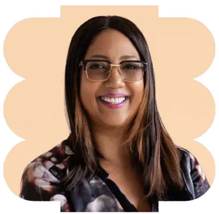 Smiling woman with long dark hair, glasses, and a floral top, posing for a portrait against a beige background.