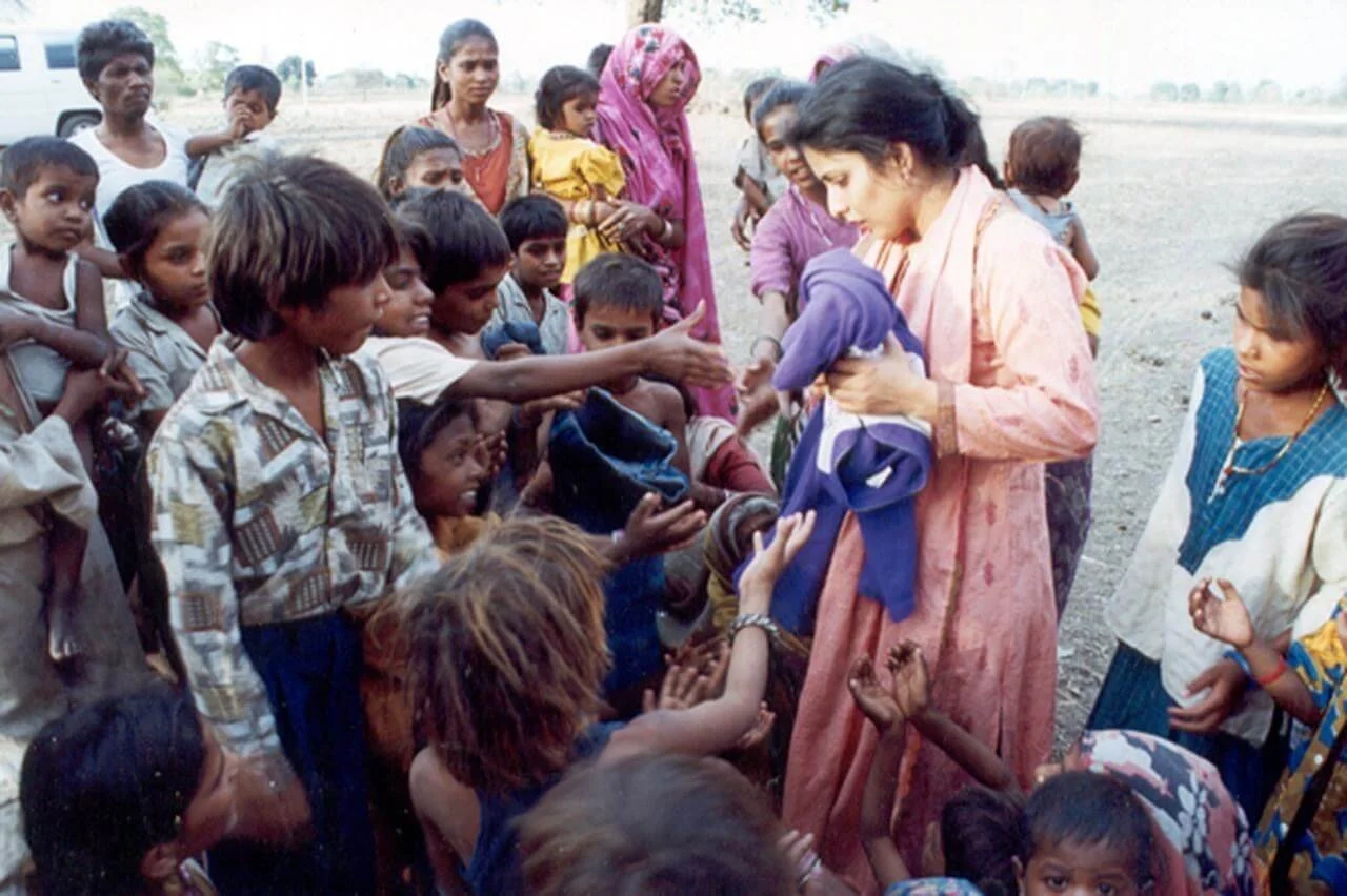 A woman in traditional attire distributing clothes to children and adults in an outdoor rural setting.
