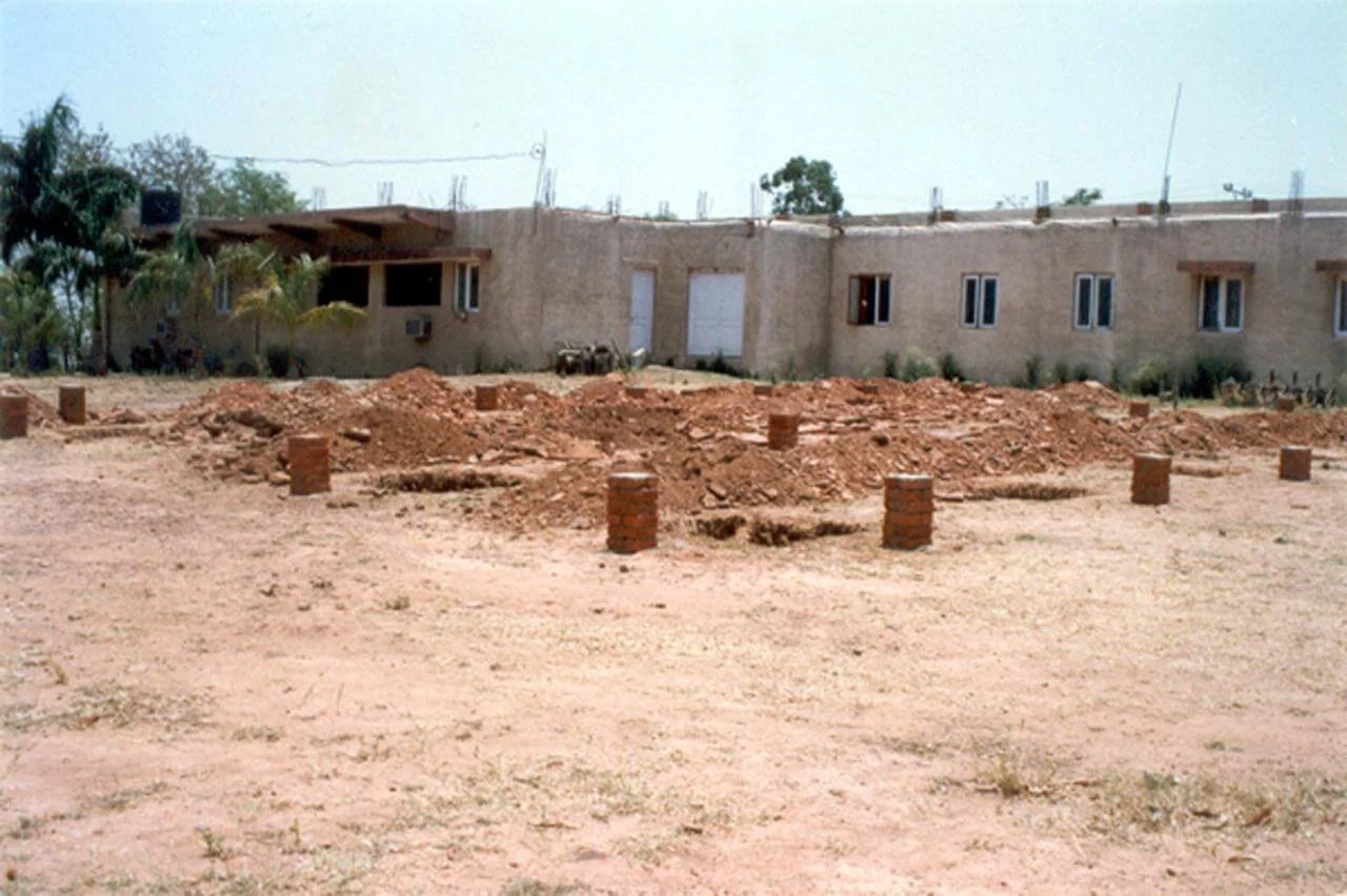 Construction site with a partially built single-story brick building in the background and dirt ground with scattered bricks in the foreground.