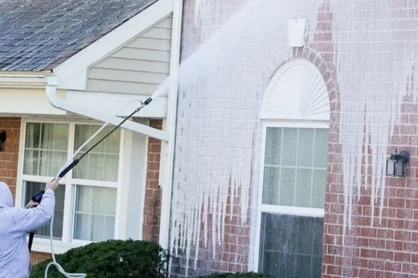 Person using a pressure washer to clean the exterior brick wall of a house.