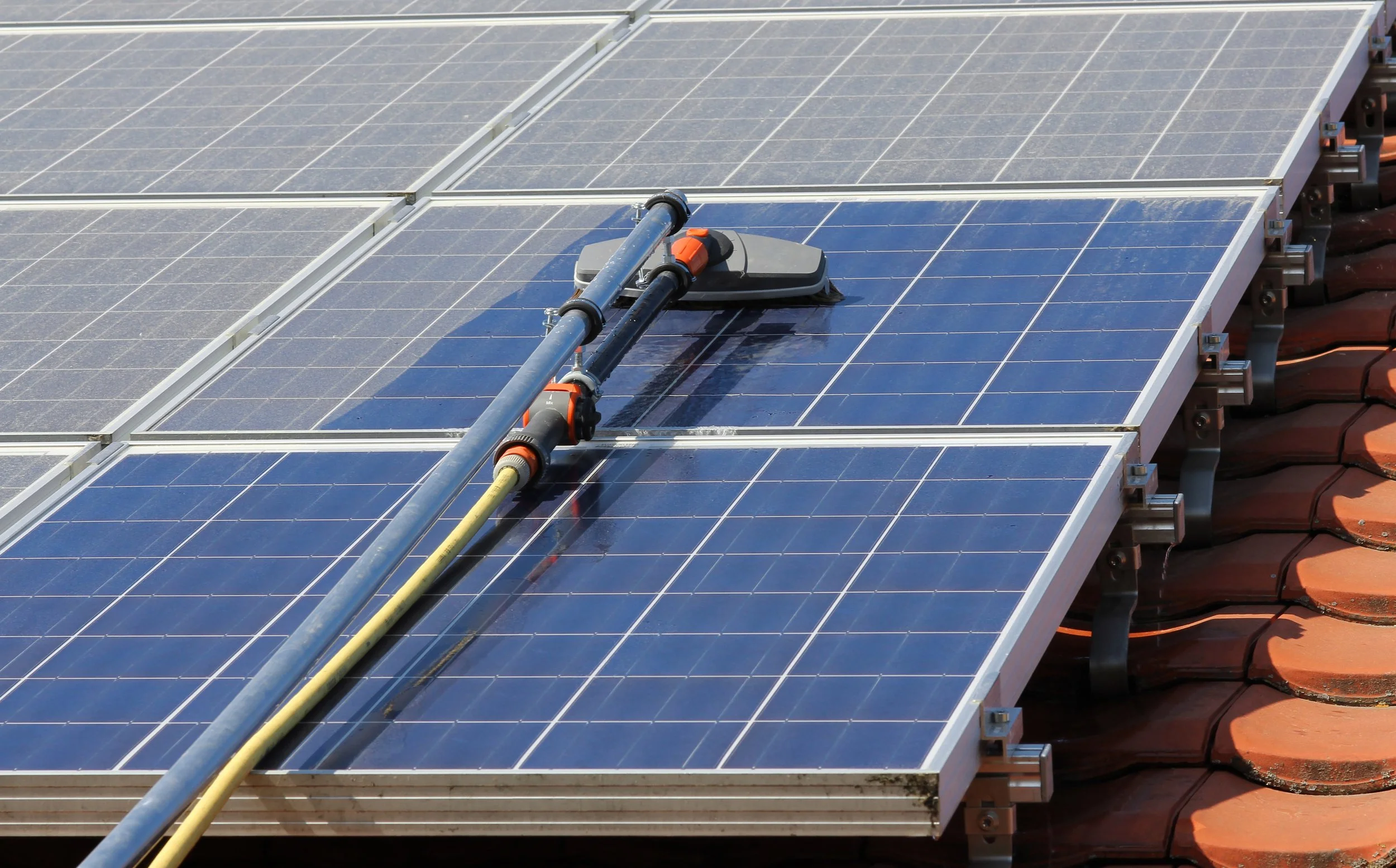 Solar panels on a roof being cleaned with a water hose