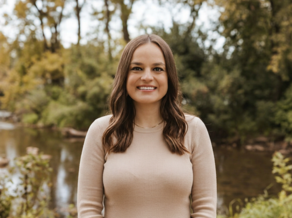 Girl smiling outdoors near a river with trees in the background.