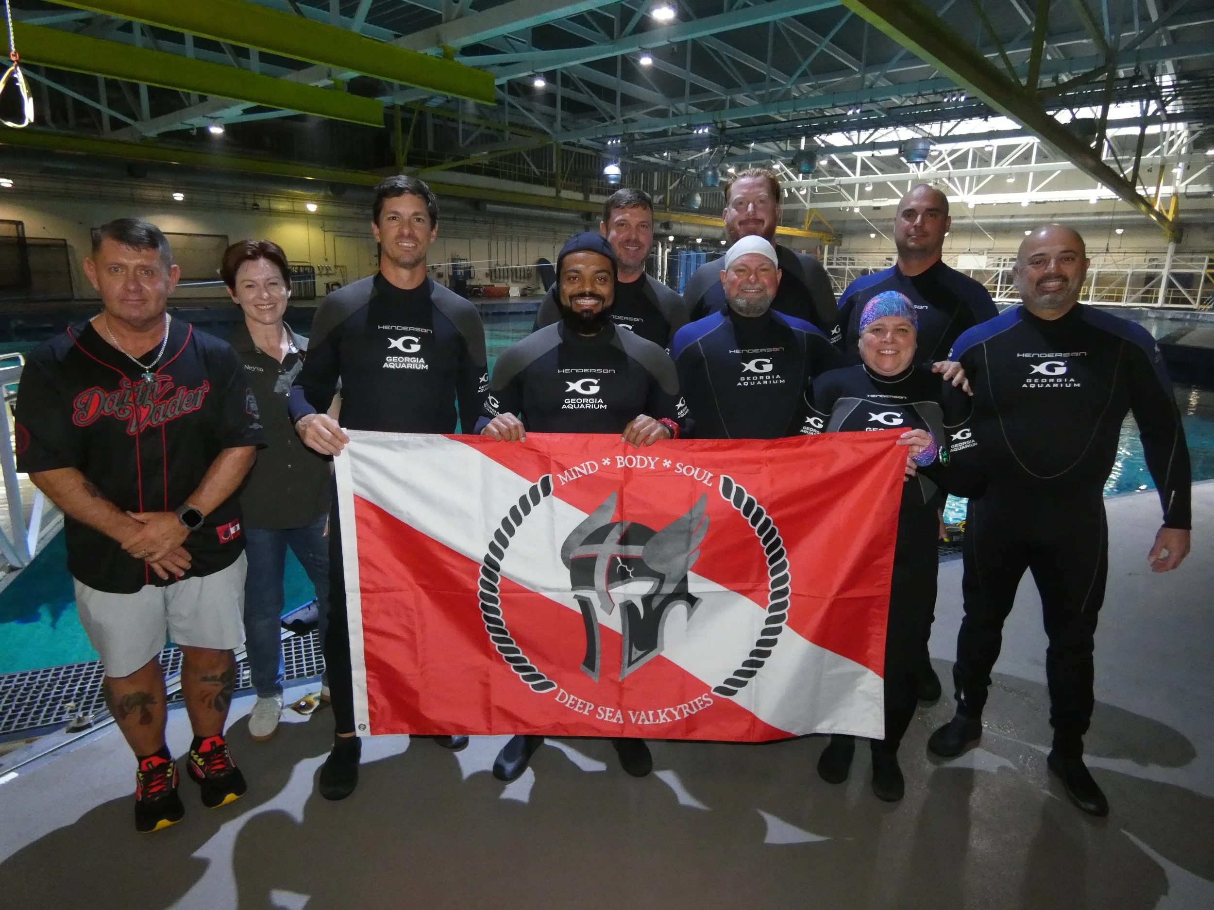 8 men and 2 women standing in front of aquarium pool holding flag with Deep Sea Valkyries logo