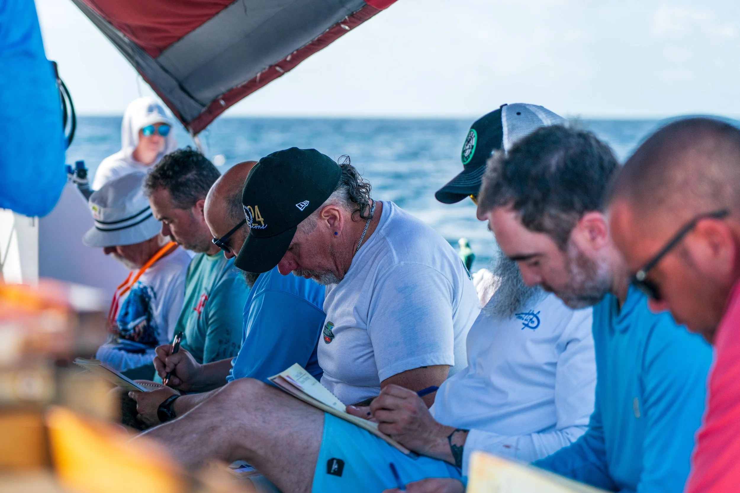 Group of people sitting on a boat, taking notes, with the ocean in the background and a small island visible on the horizon.
