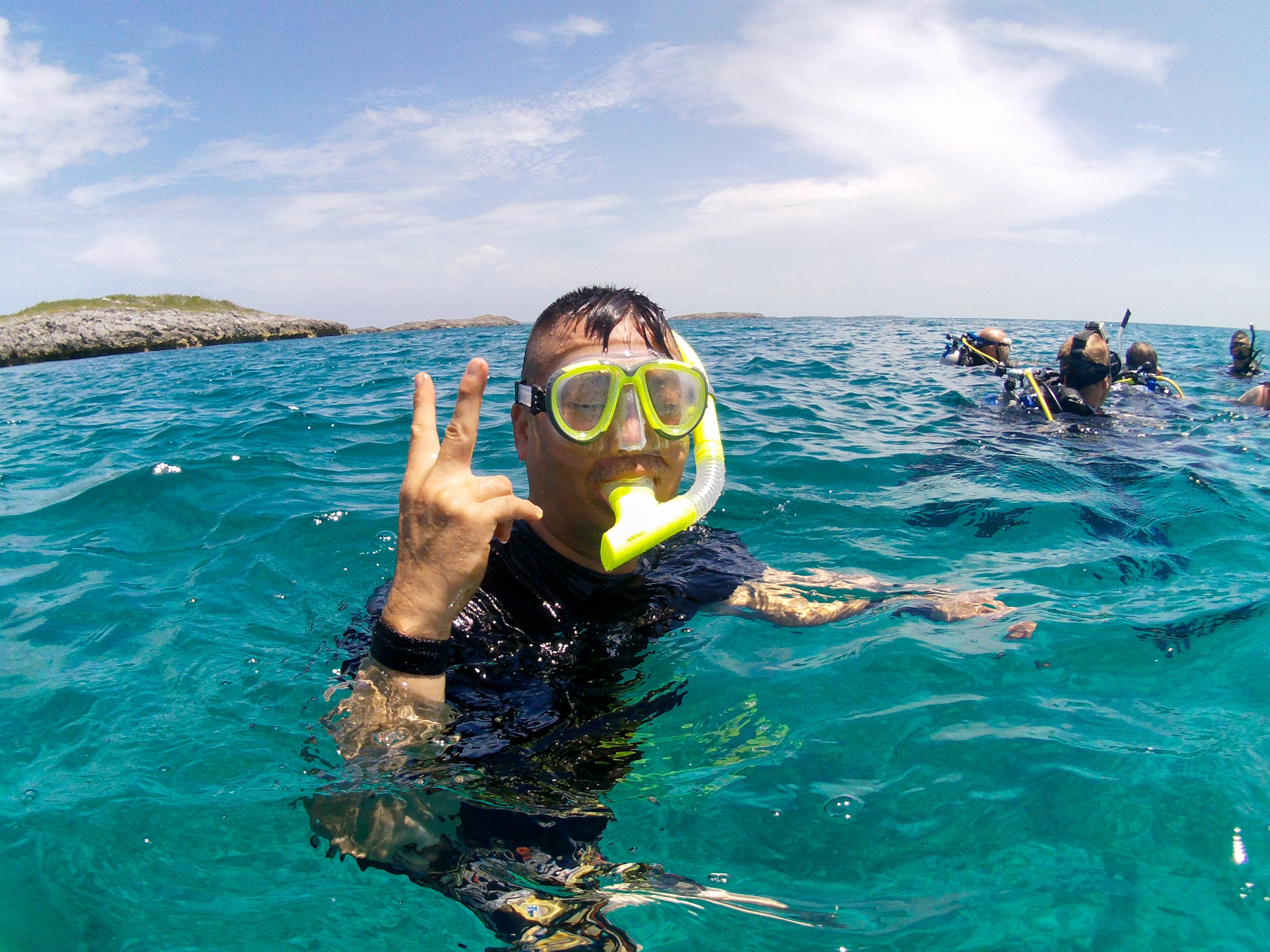 Person in snorkeling gear giving a peace sign in the ocean with a group of snorkelers in the background.