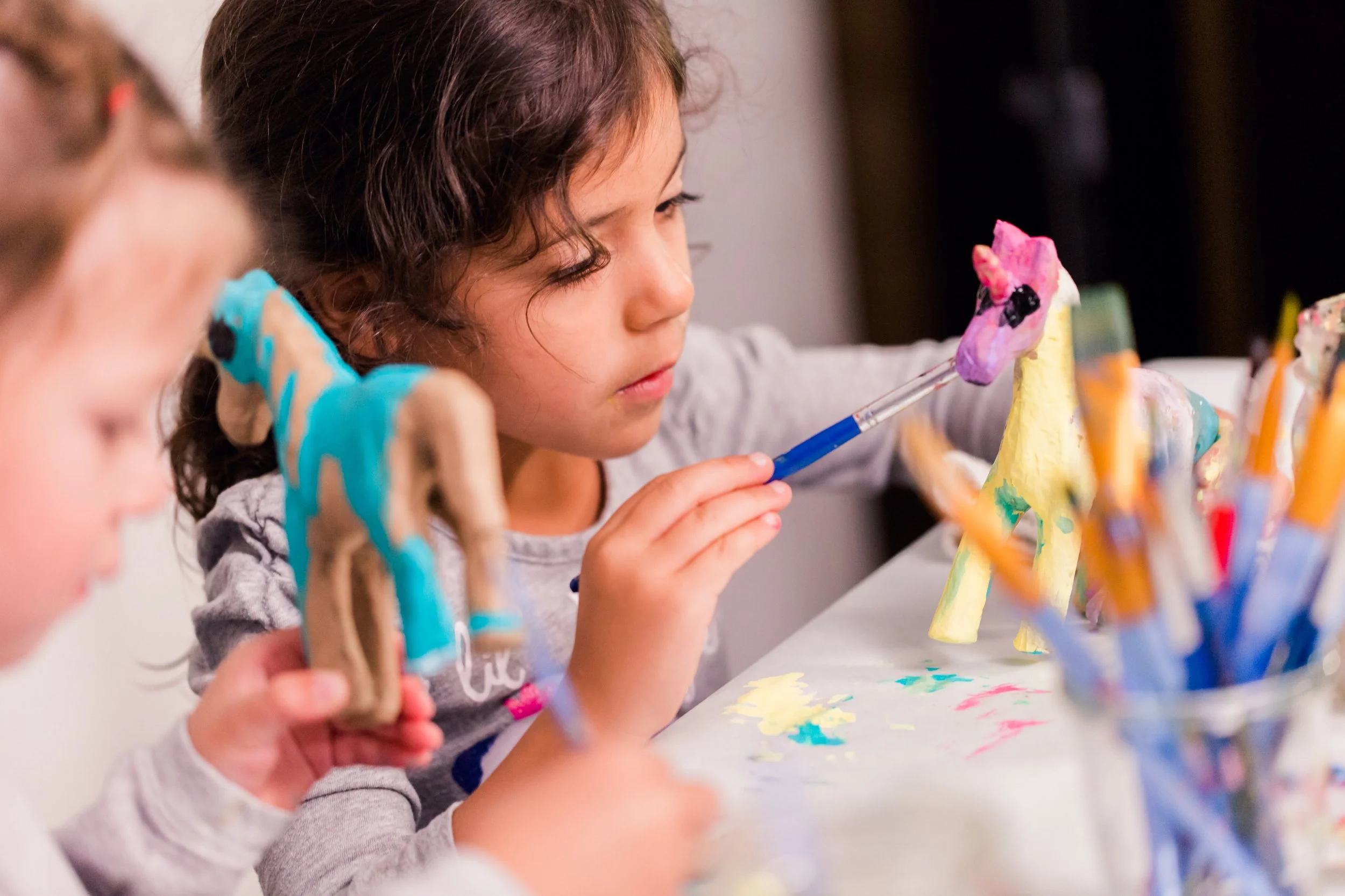 A girl with curly hair painting a unicorn figurine with colorful paints