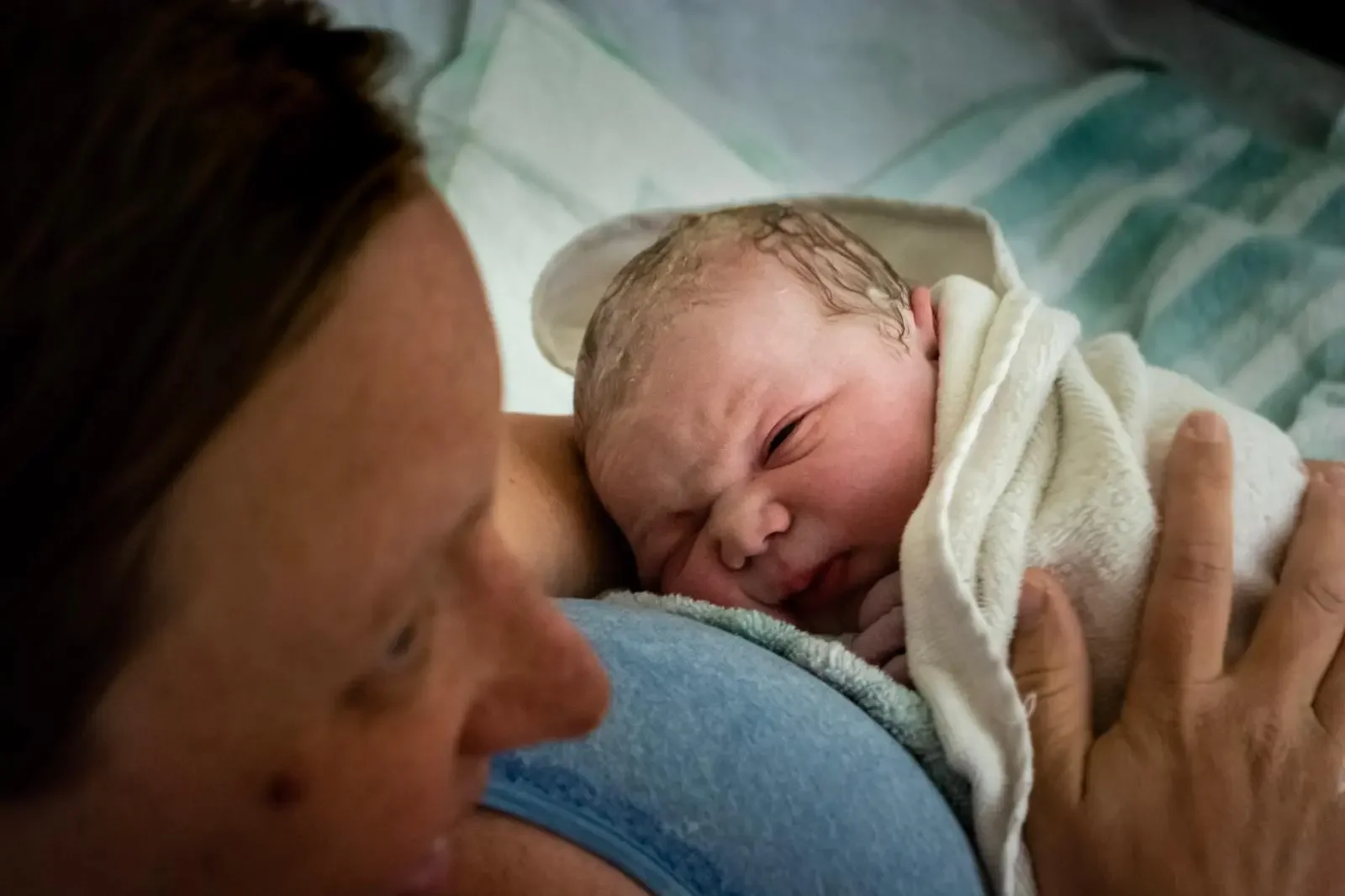 Picture of a newborn baby having just been birthed at home, looking up at his mother