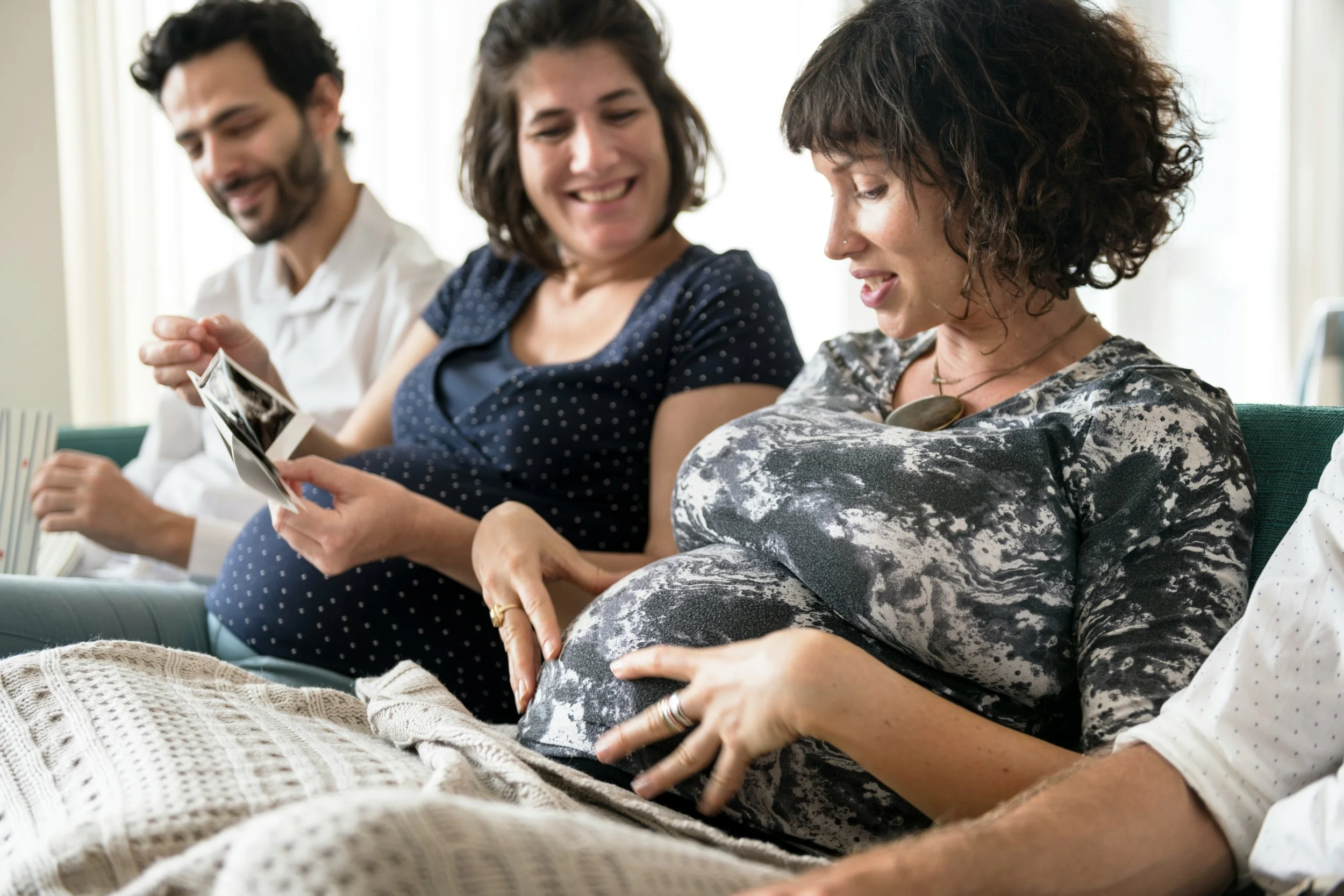 Three people sitting together indoors, one woman holding an ultrasound image, and they are smiling and looking at it.