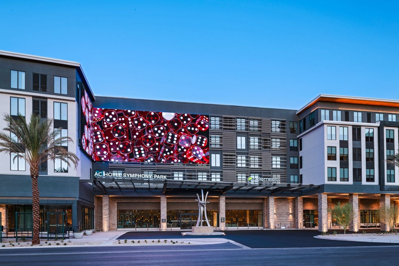 Modern hotel building with palm trees in front, street signs, and street lamps against a clear blue sky.