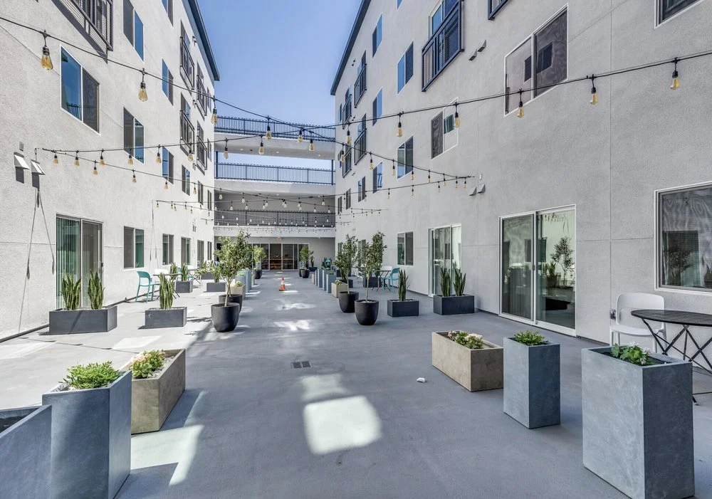 Modern white apartment building with multiple balconies and large windows under a clear blue sky.