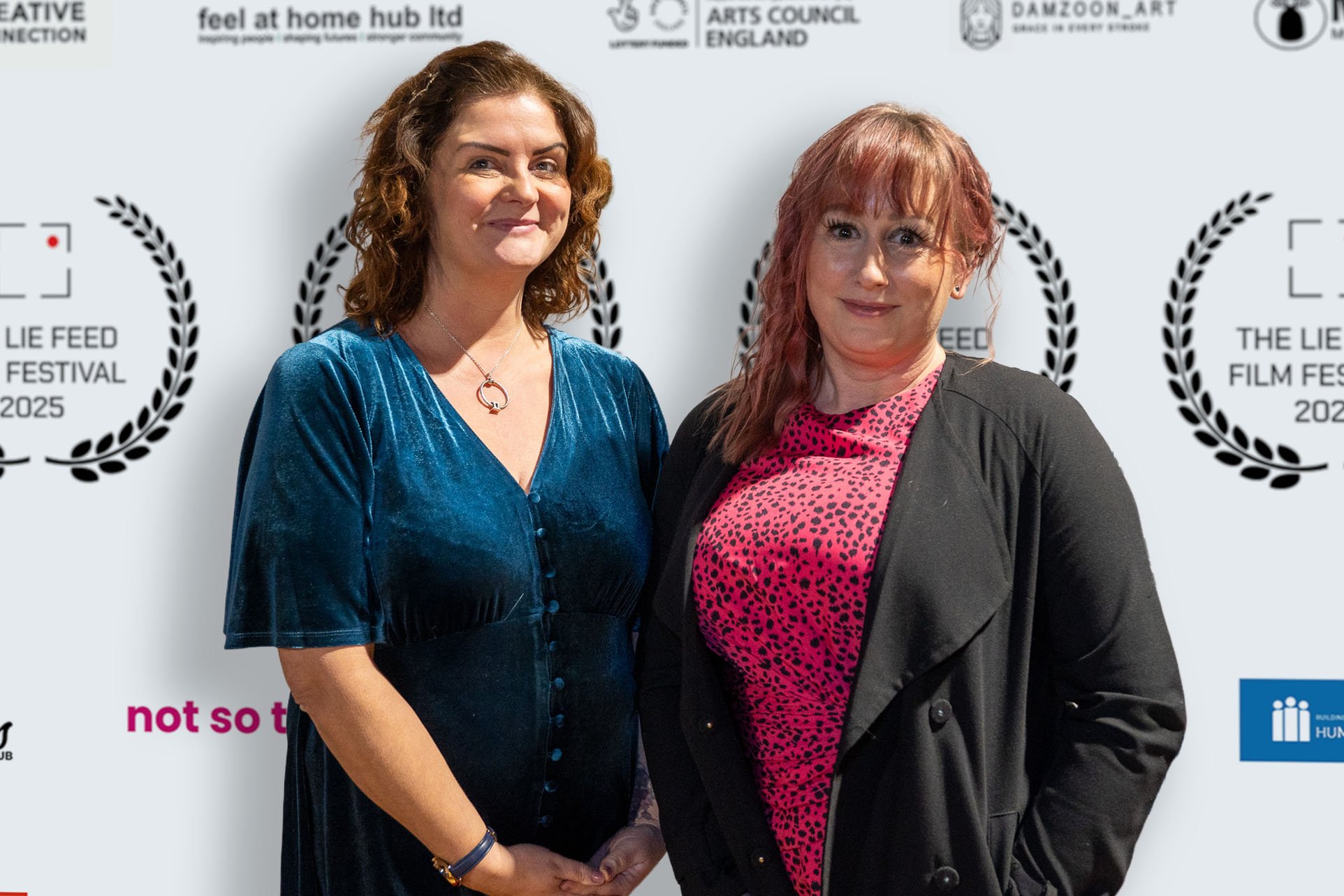 Two women standing together at the Lie Feed Festival 2025, smiling and posing for a photo in front of a backdrop featuring logos and text related to the event.