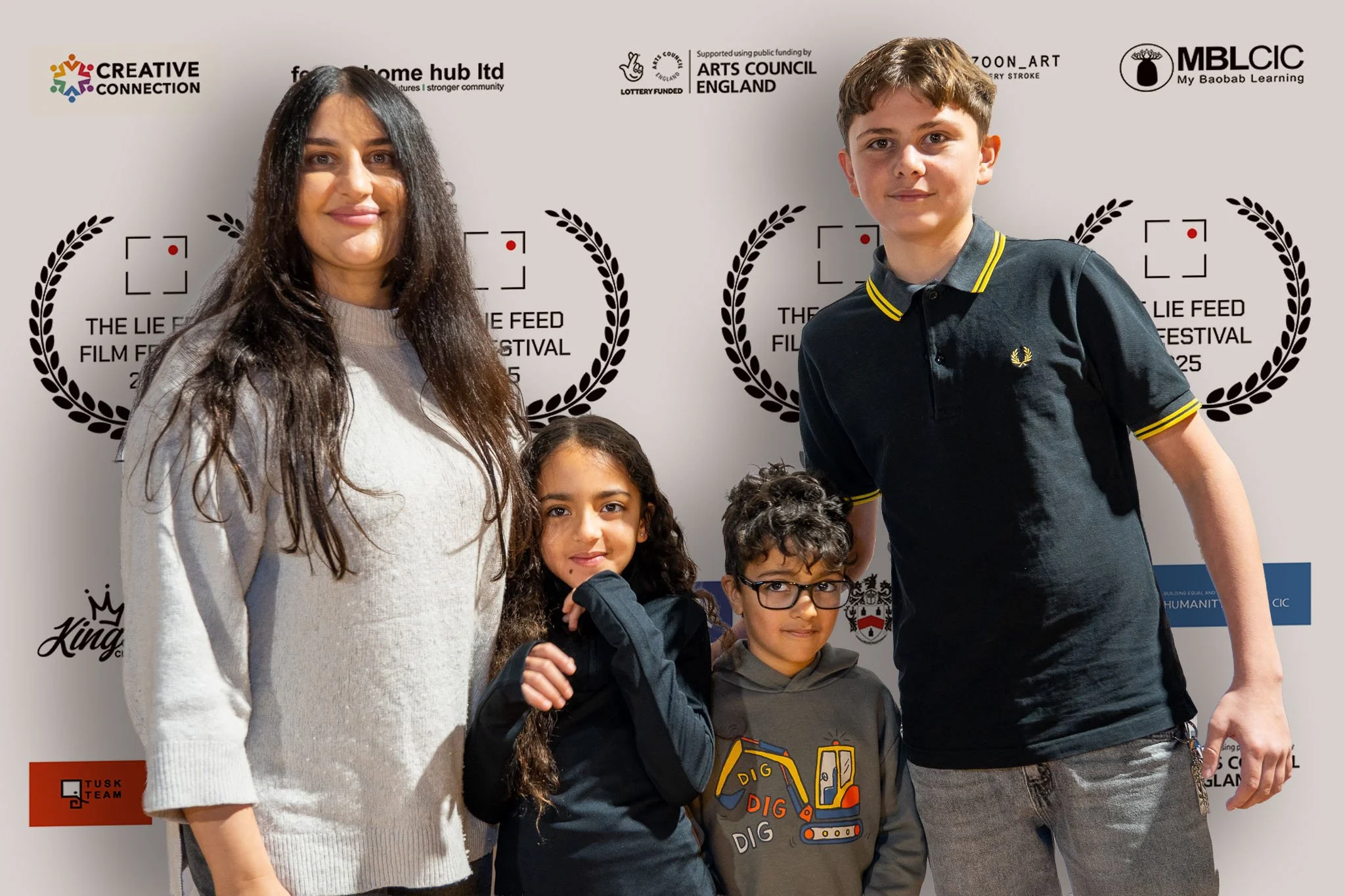 Group of four children and a woman standing in front of a white backdrop with logos and text for a film festival, smiling at the camera.