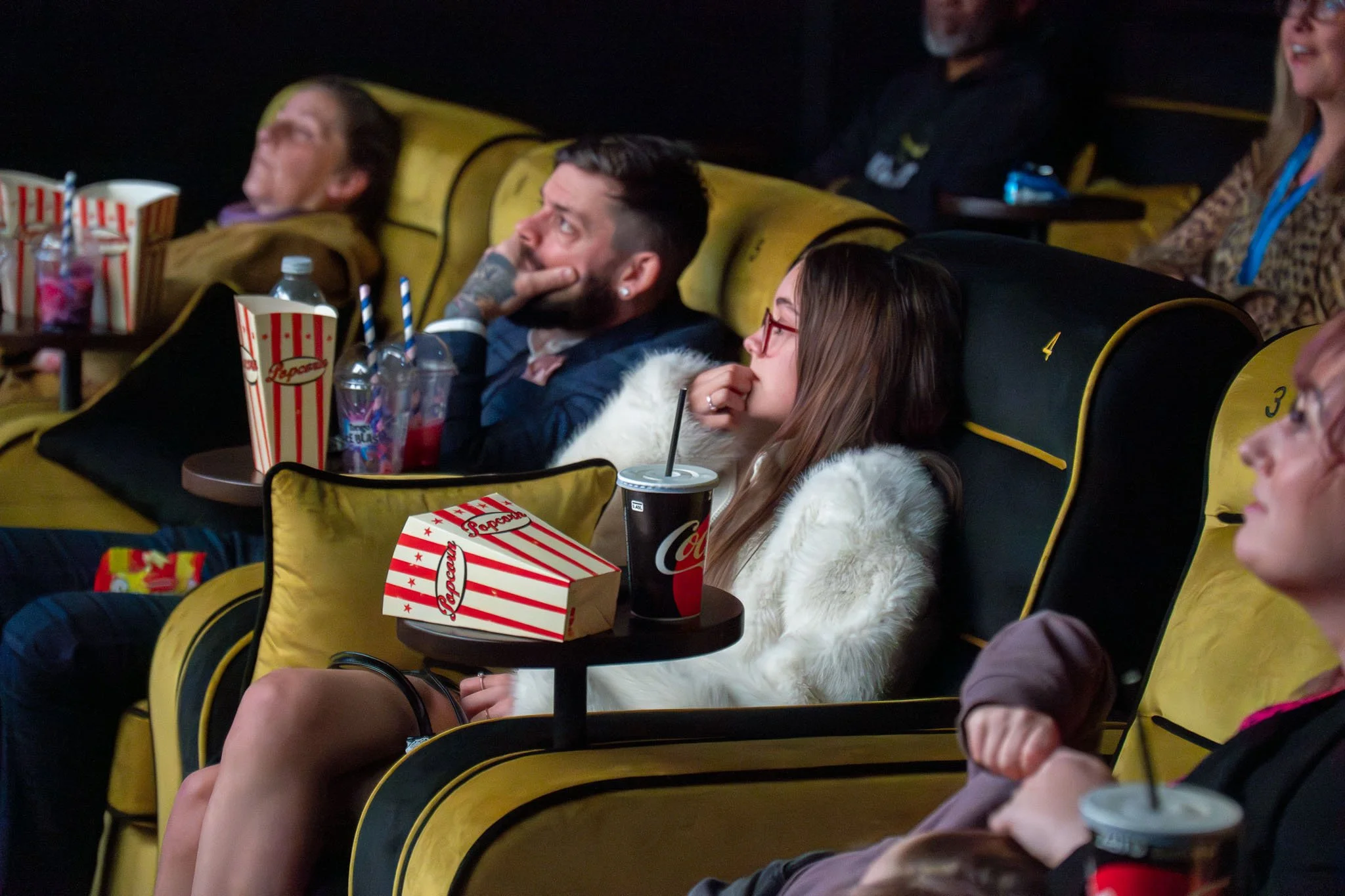 People sitting in theater seats watching a movie, with popcorn and sodas.
