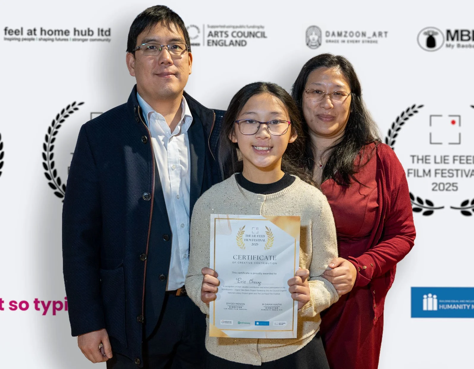 Young girl holding a certificate, standing between two adults, at the Lie Feed Film Festival 2025 event, with logos and text on the backdrop.