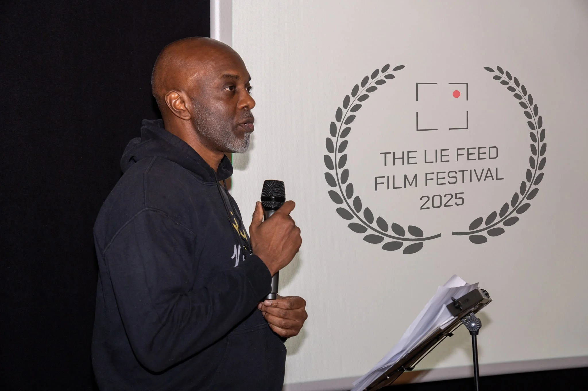 Man speaking into a microphone at The Lie Feed Film Festival 2025.