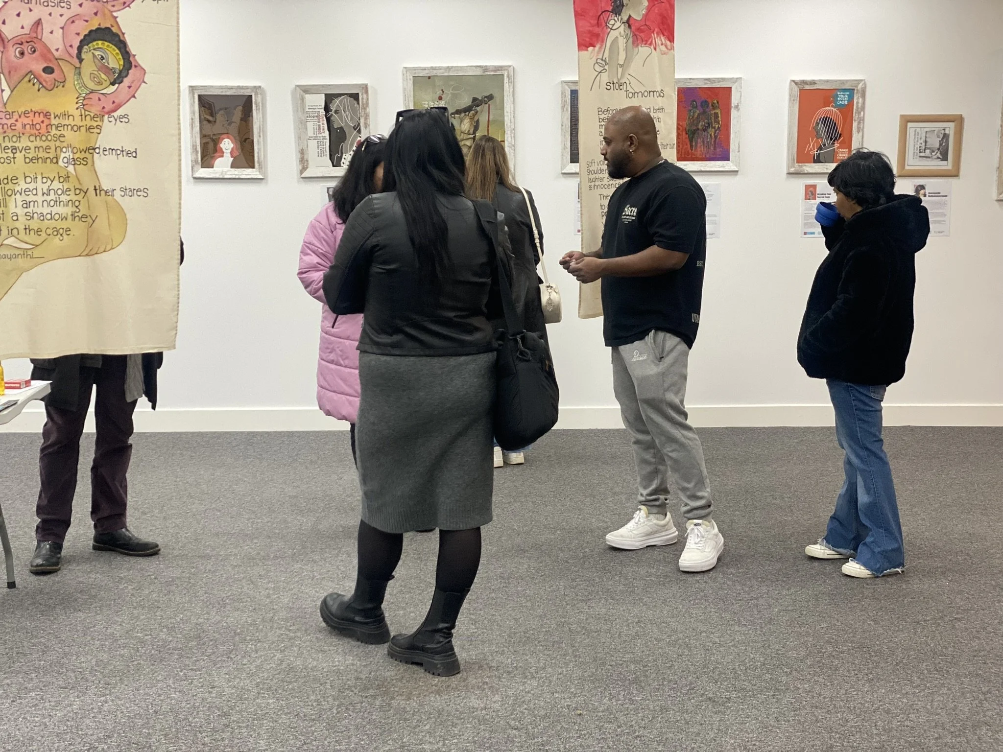 Group of visitors inside an art gallery observing artwork on the wall, with some engaging in conversation.