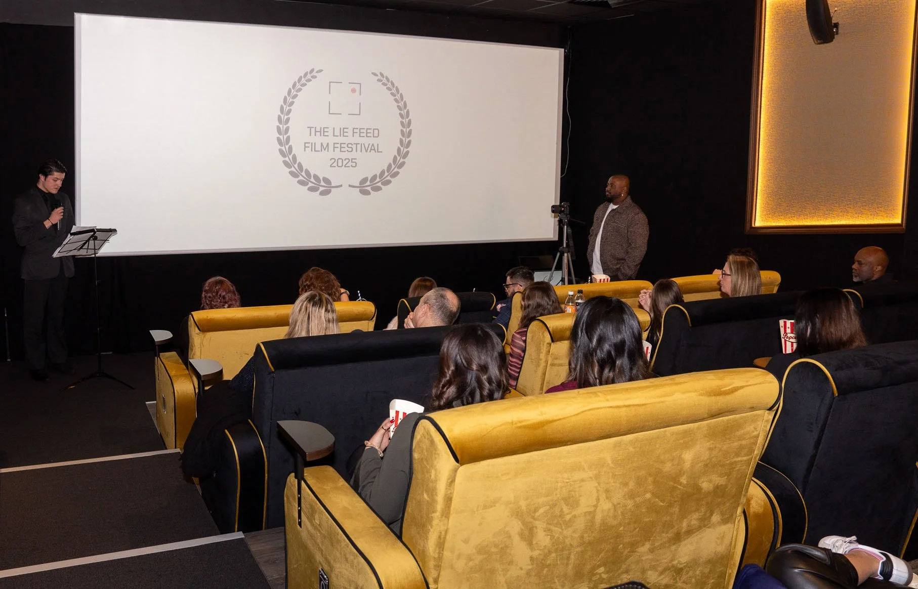 Audience seated in a theater watching a presentation on screen that displays the logo for The Lie Feed Film Festival 2025