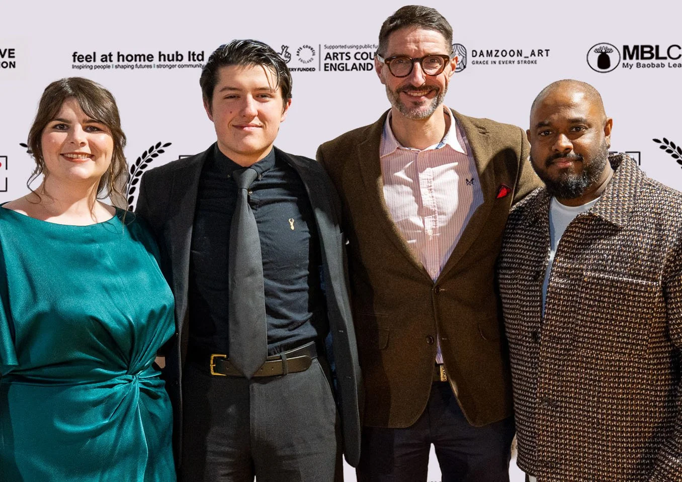 Four people standing together at an event with a step and repeat backdrop featuring logos and sponsors.