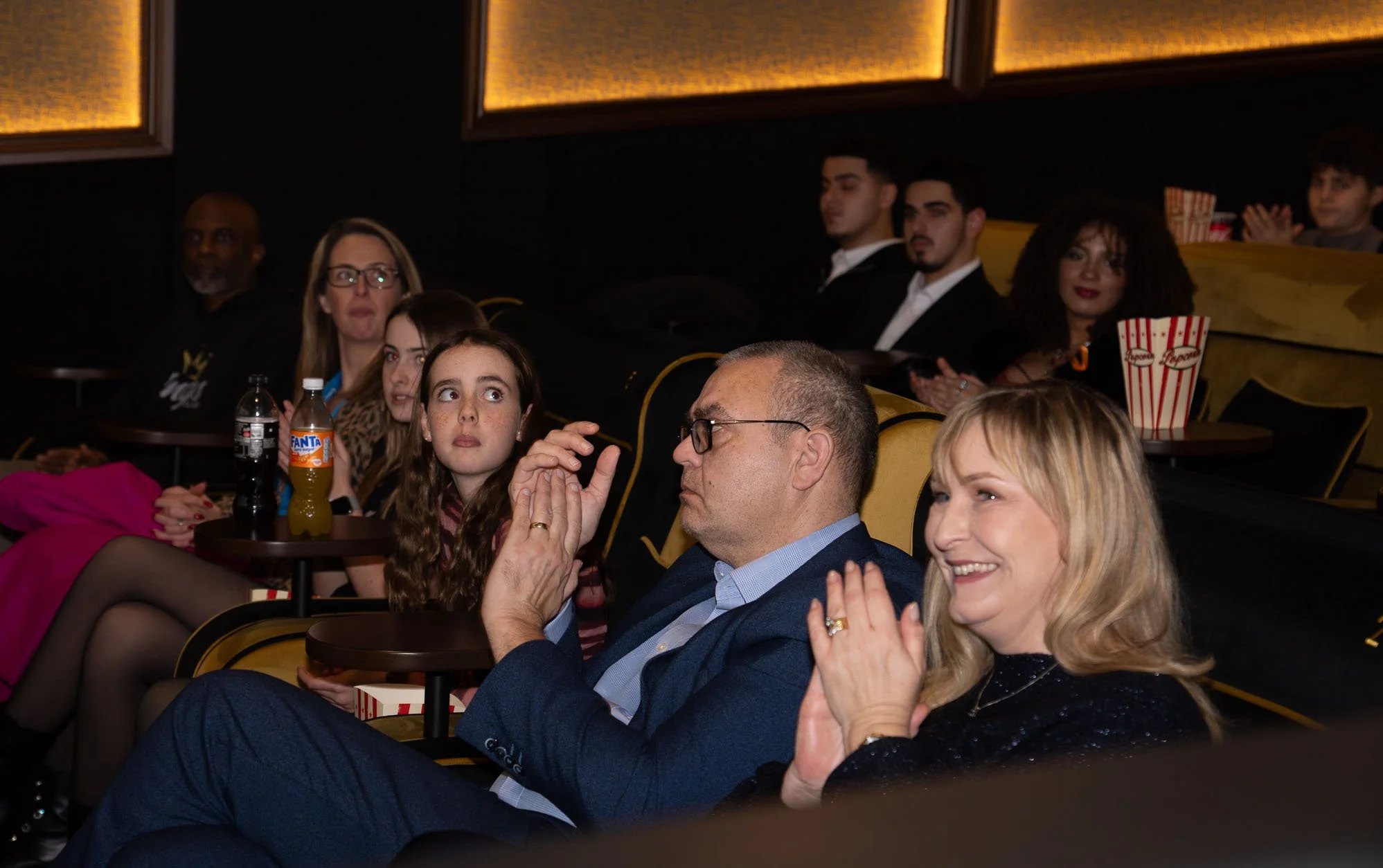 A group of people sitting in a movie theater, watching the screen with focused, entertained, and smiling expressions.