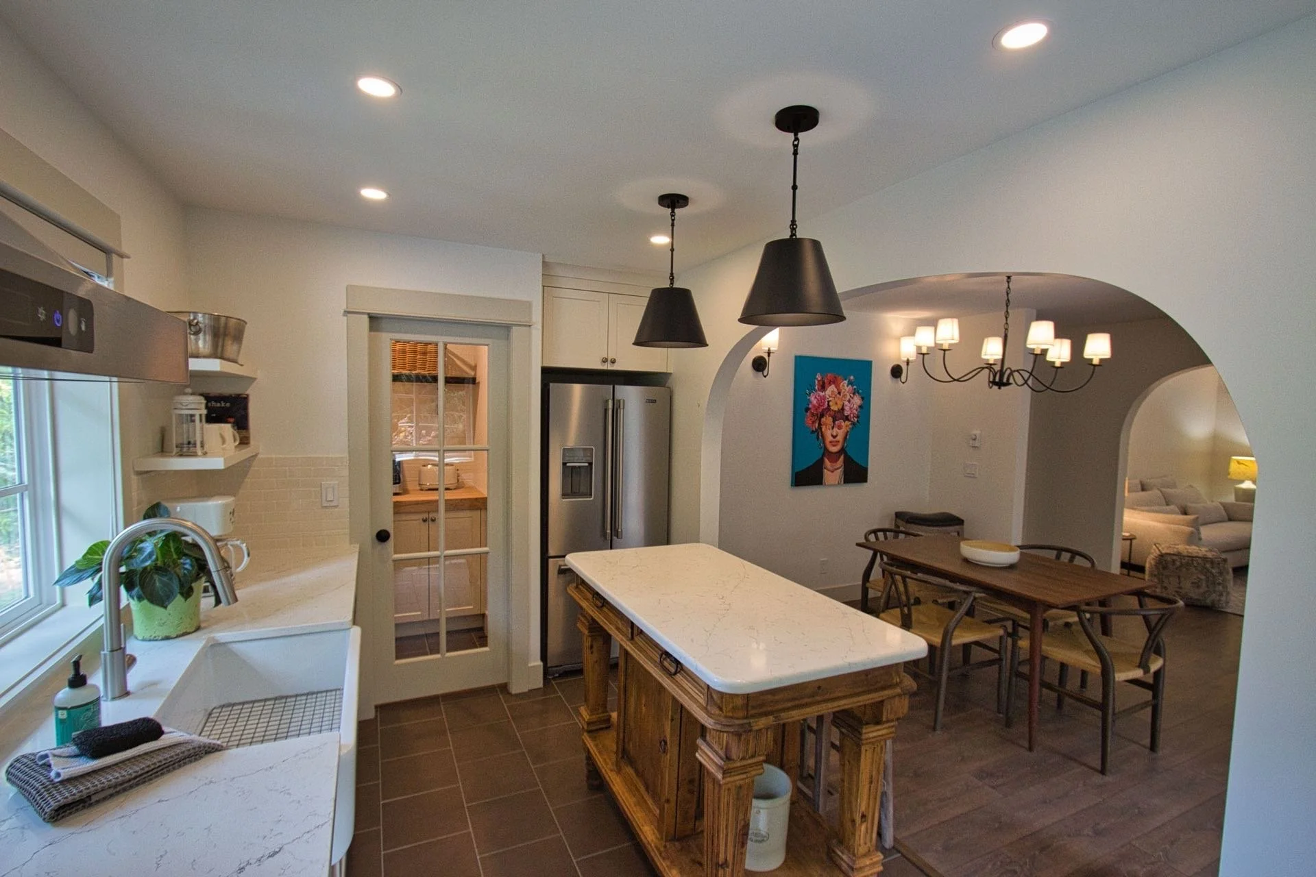 Kitchen with a white marble island, stainless steel refrigerator, black pendant lights, and wall art featuring a woman with floral headpiece in the dining area