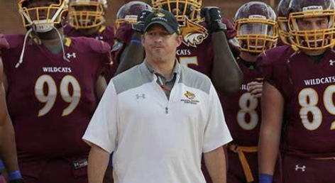 A football coach standing with his team of players in maroon uniforms with yellow helmets outdoors.