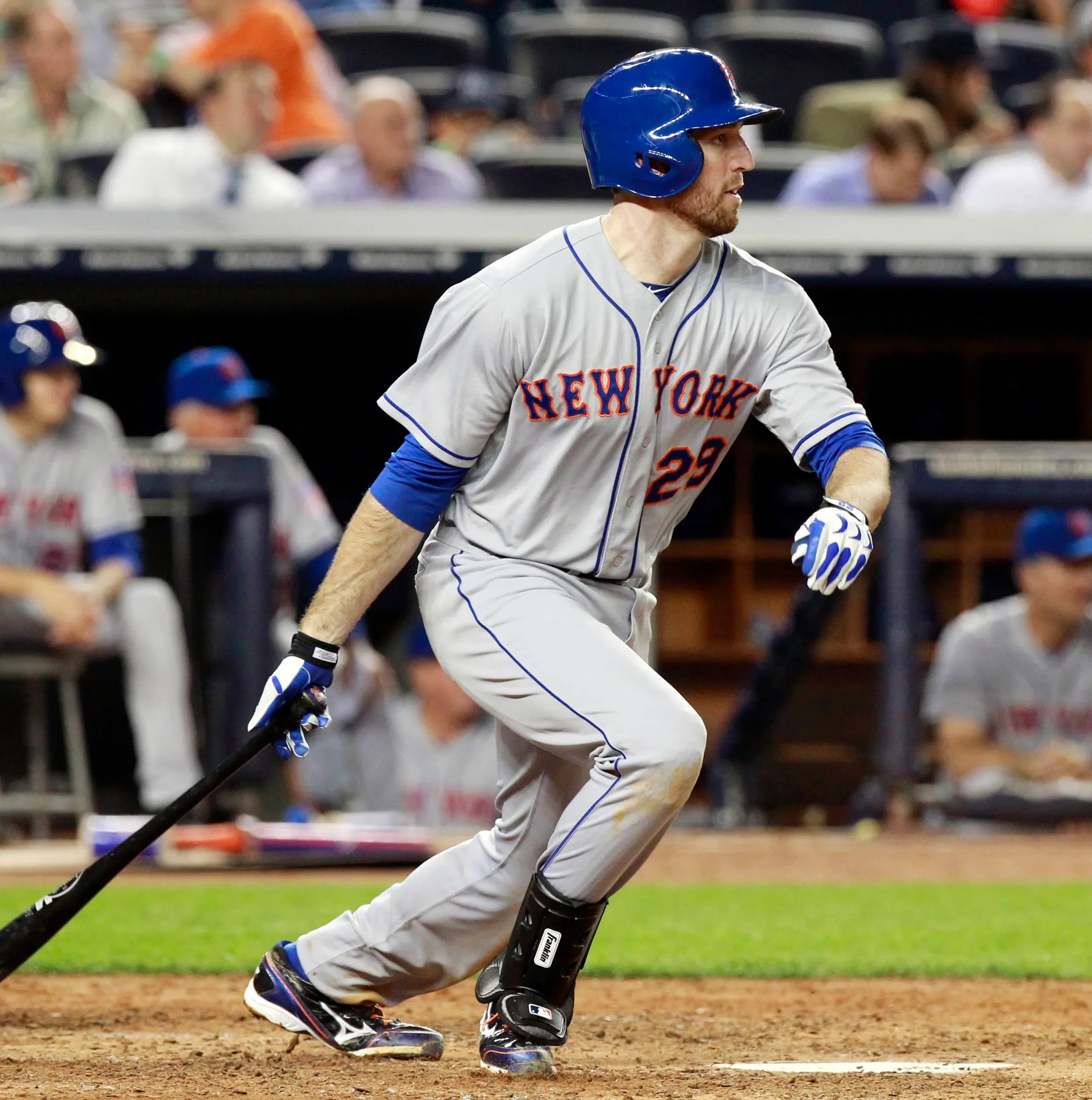 A baseball player from the New York team running on the field during a game, wearing a gray uniform with blue and red accents and a blue helmet