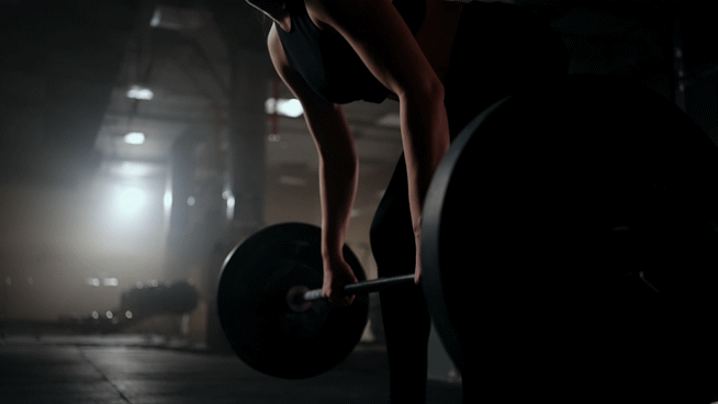 A person performing a deadlift exercise in a gym with dim lighting.