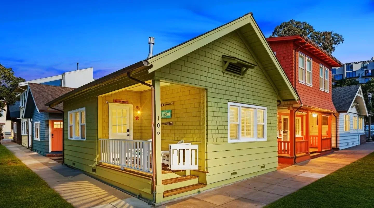 Colorful houses in a neighborhood at dusk, with lit windows and streetlights, featuring yellow, red, blue, and white exteriors.