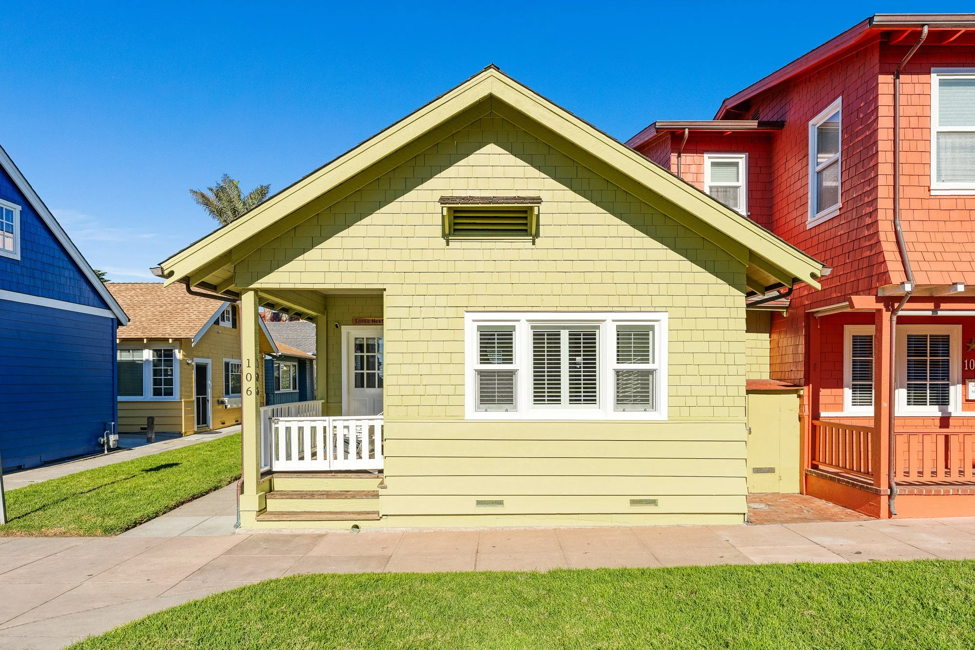 Colorful house with a yellow exterior and white window trim, flanked by blue and red houses, under a clear blue sky.