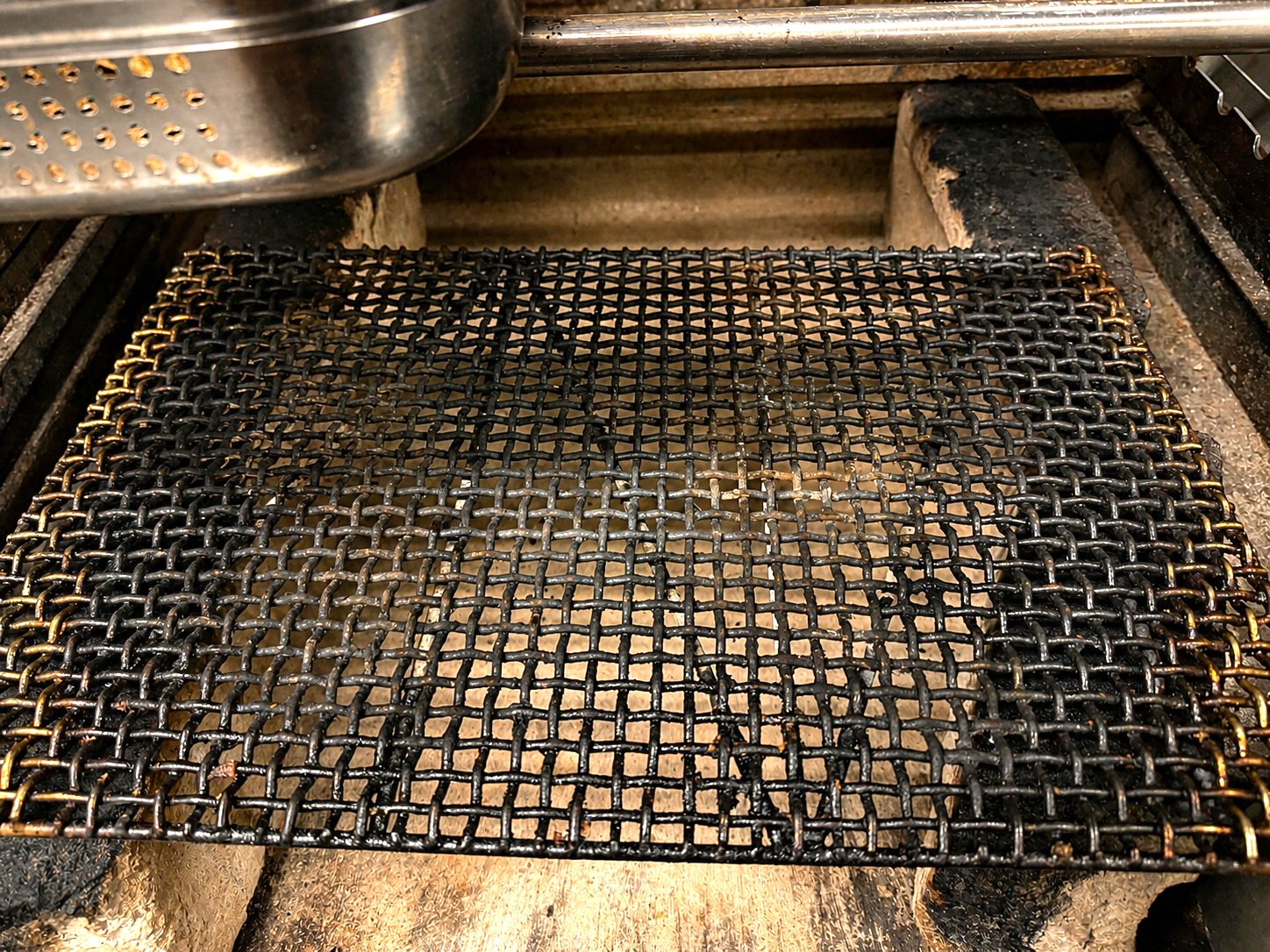 A metal grilling grate placed over hot coals in a barbecue grill.