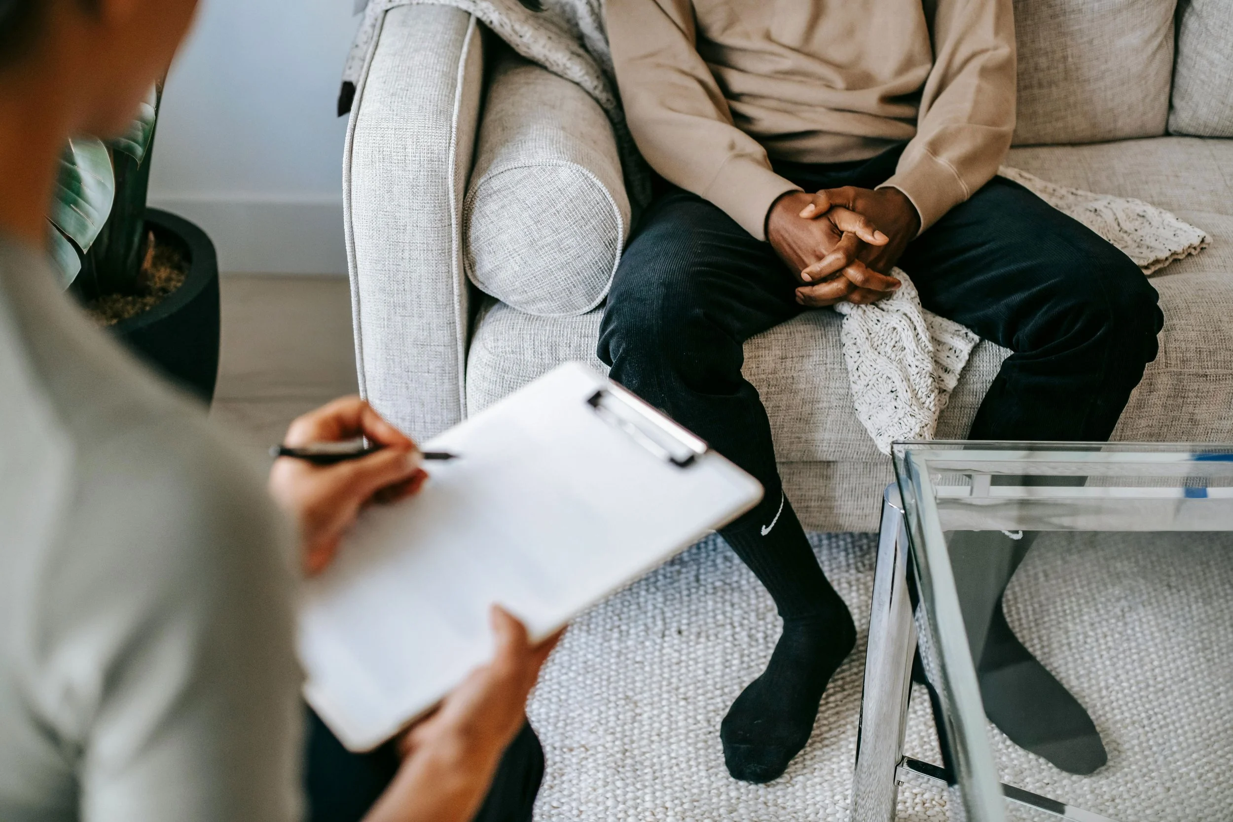 Person sitting on a gray couch during a medical intake session, with a doctor taking notes on a clipboard.