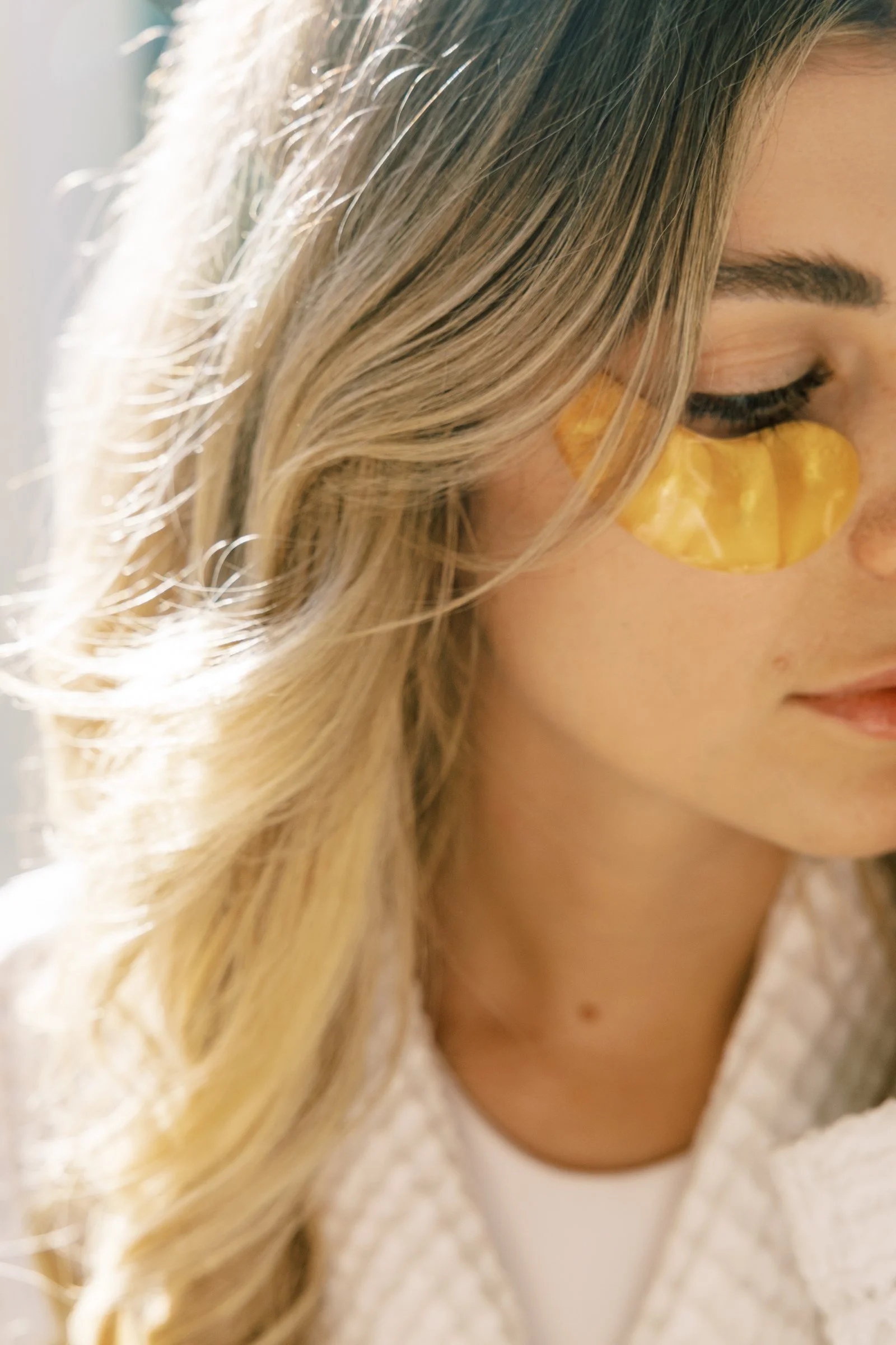 A woman with blonde hair and eye makeup, with gold eye patches under her eyes, facing slightly right.