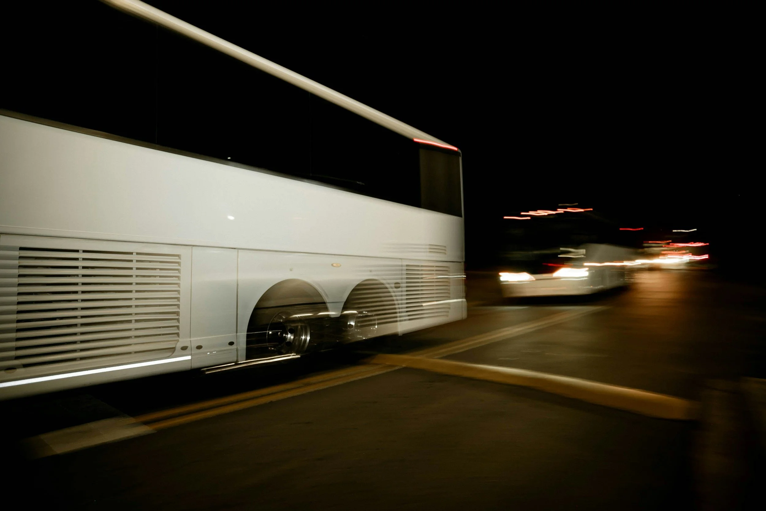 Nighttime scene of a large white bus with blurred lights in the background, indicating motion.