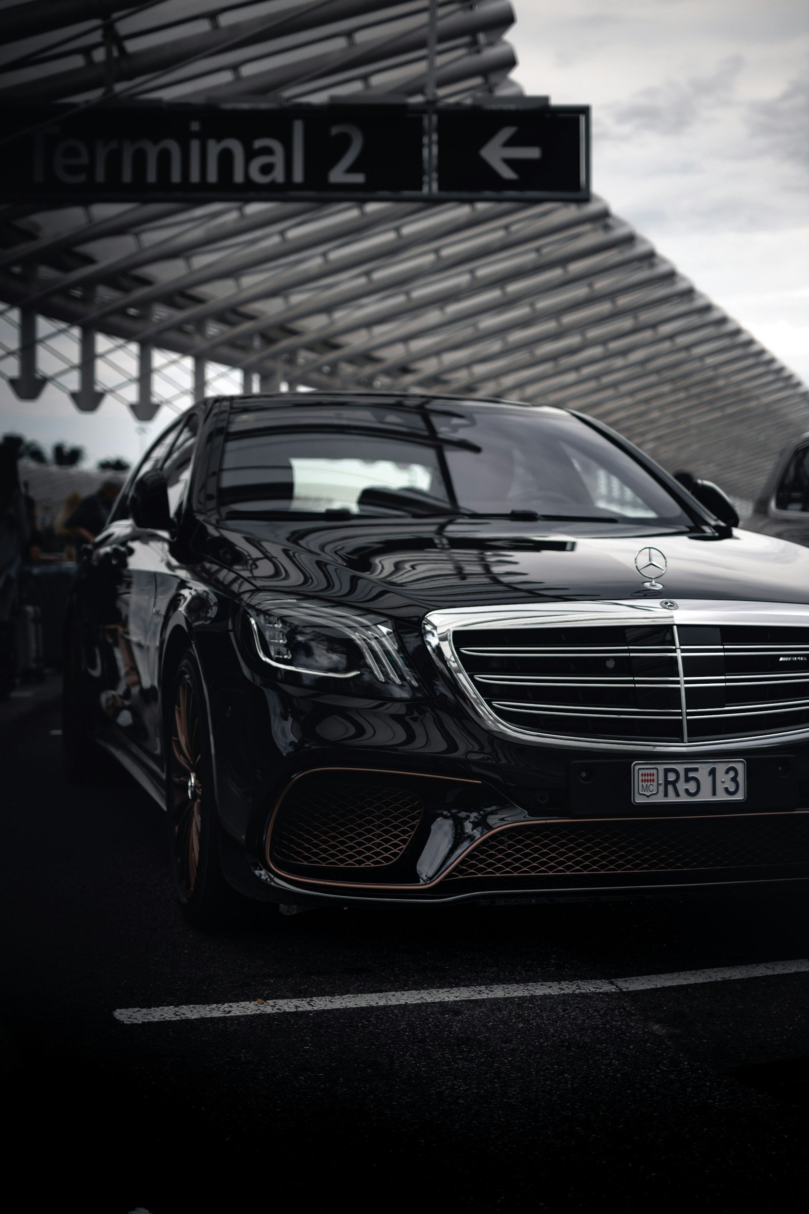 Black Mercedes-Benz sedan parked at an airport terminal with a 'Terminal 2' sign overhead.
