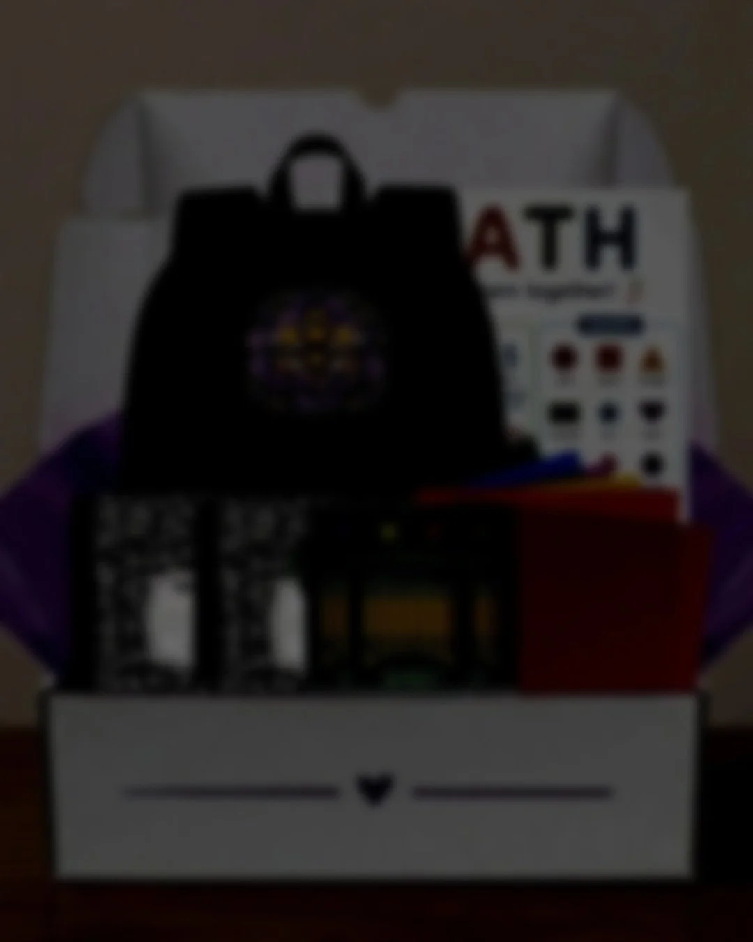 Back-to-school supply gift box including a small black backpack with a colorful bee and flower design, a learning poster about shapes, notebooks, colored paper, yellow pencils, and contact paper in a white box with purple heart decorations.