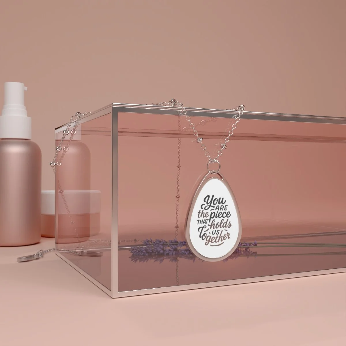 A jewelry display case with a silver necklace holding a pendant featuring a quote, set against a soft pink background with lotion bottles nearby.