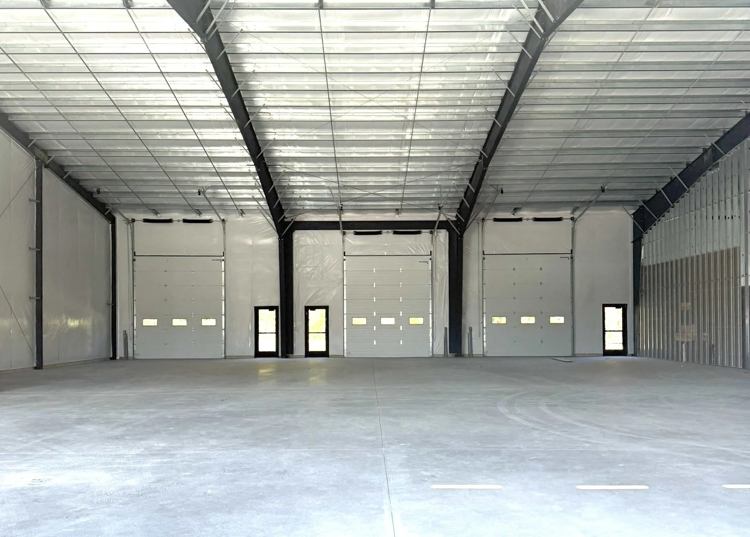 Empty indoor warehouse with three garage doors at the back and a concrete floor.