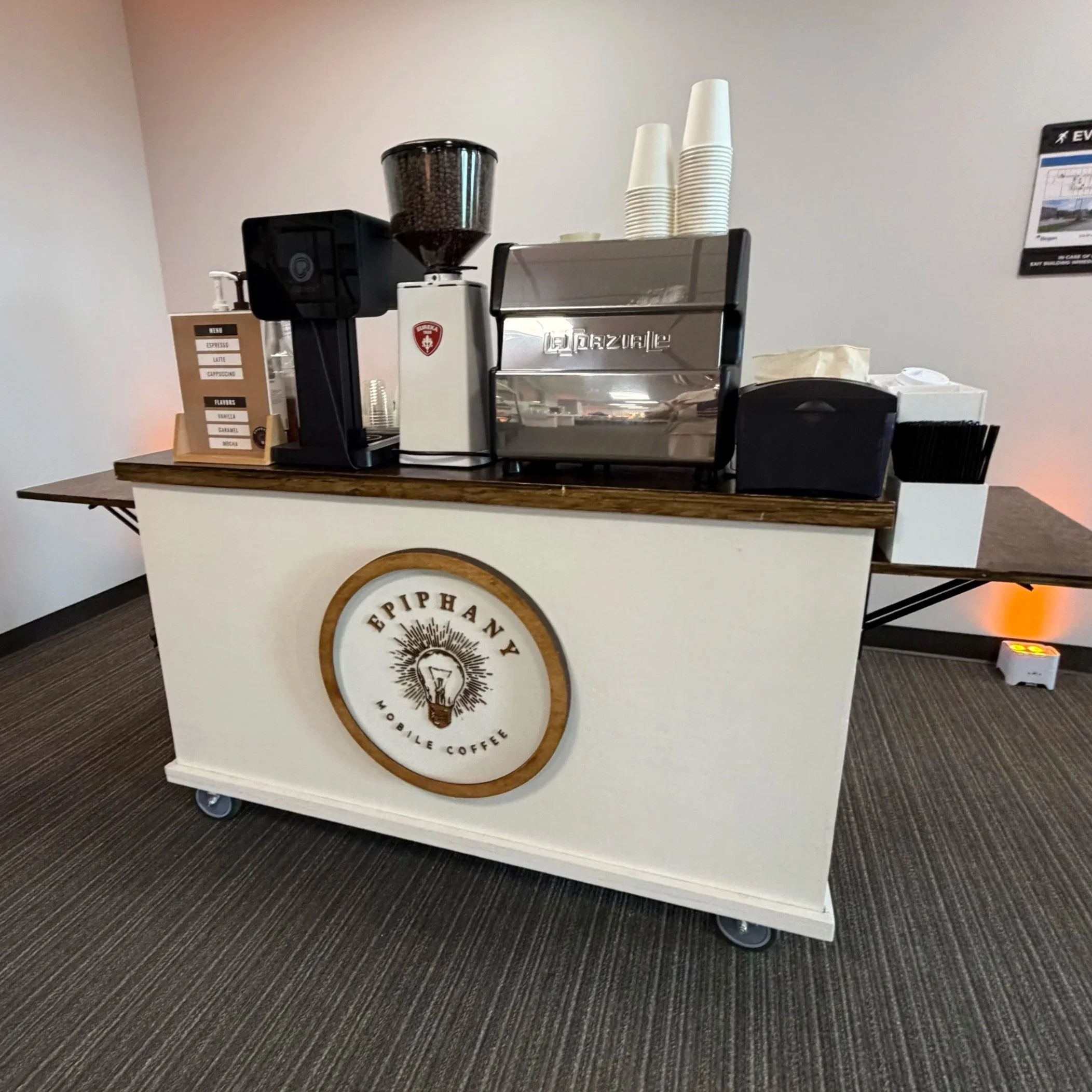 Coffee shop counter with espresso machine, coffee grinder, cups, and a menu board.