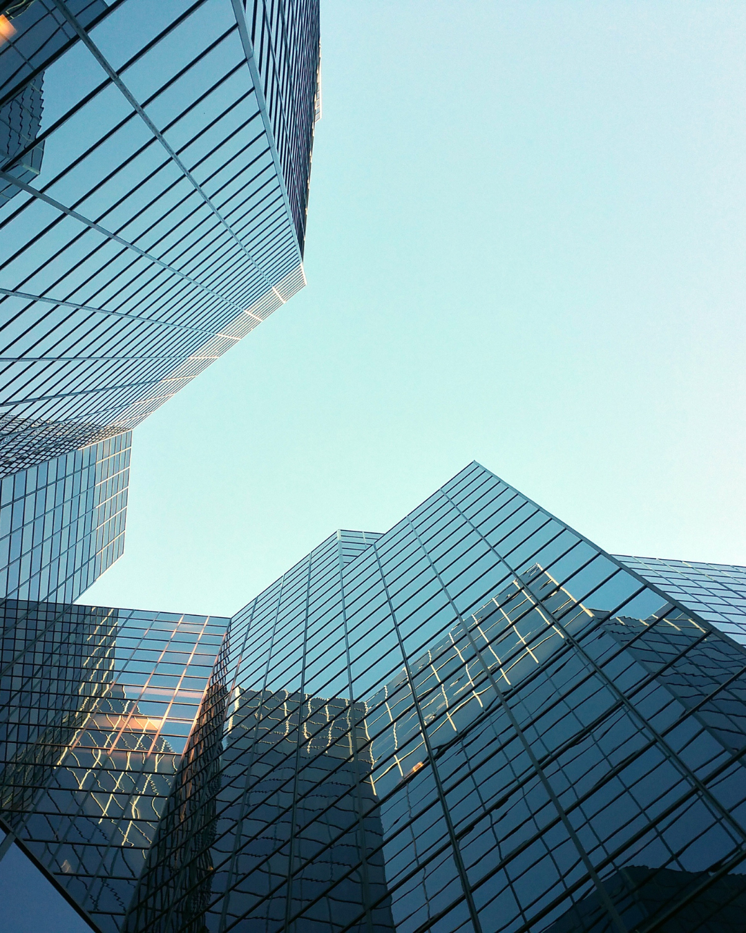 Looking up at modern glass skyscrapers reflecting the sky in an urban cityscape.