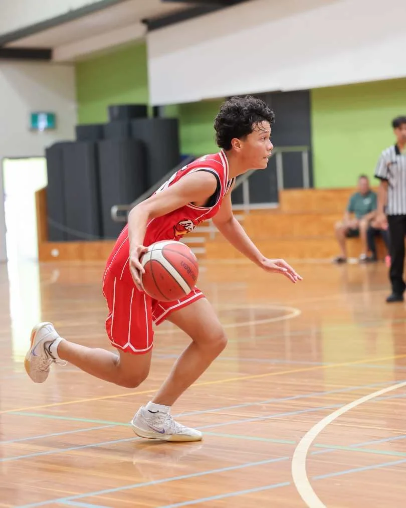 A female basketball player in a red uniform dribbling on a basketball court.