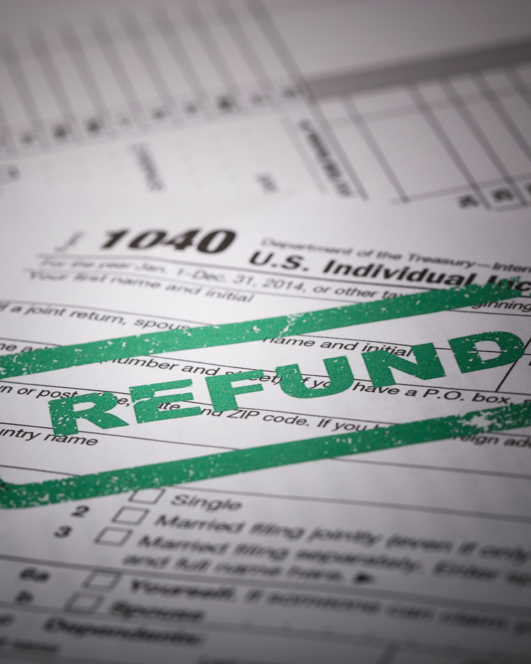 A blurry close-up of a tax form with a green stamp that says 'REFUND'.
