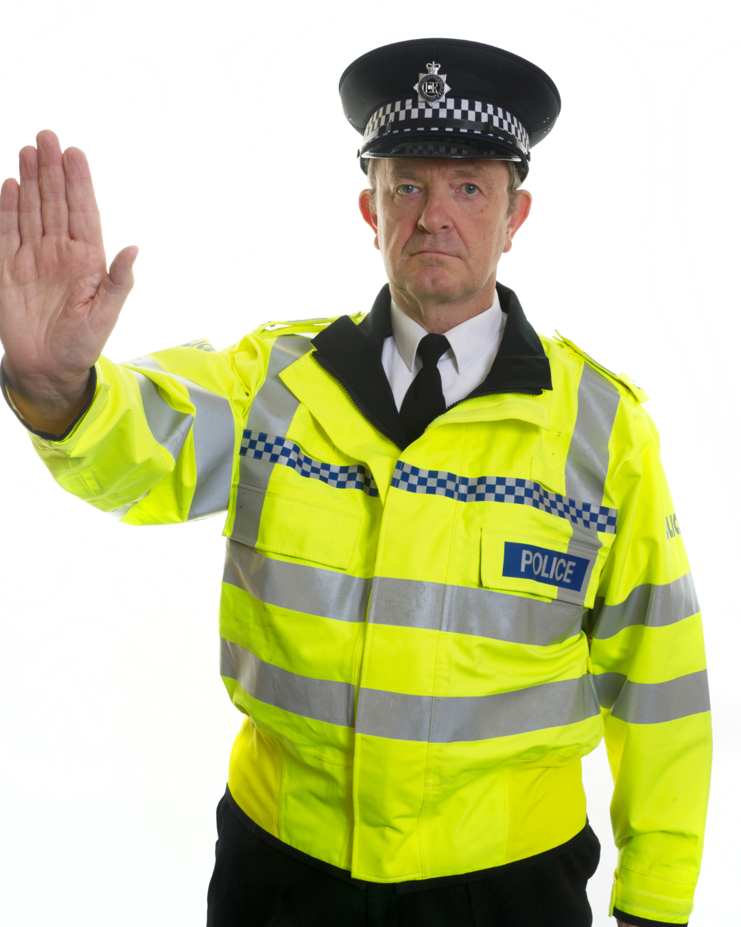 A police officer in a bright yellow jacket with reflective strips, wearing a police hat with a badge, holding up his hand in a stop gesture.