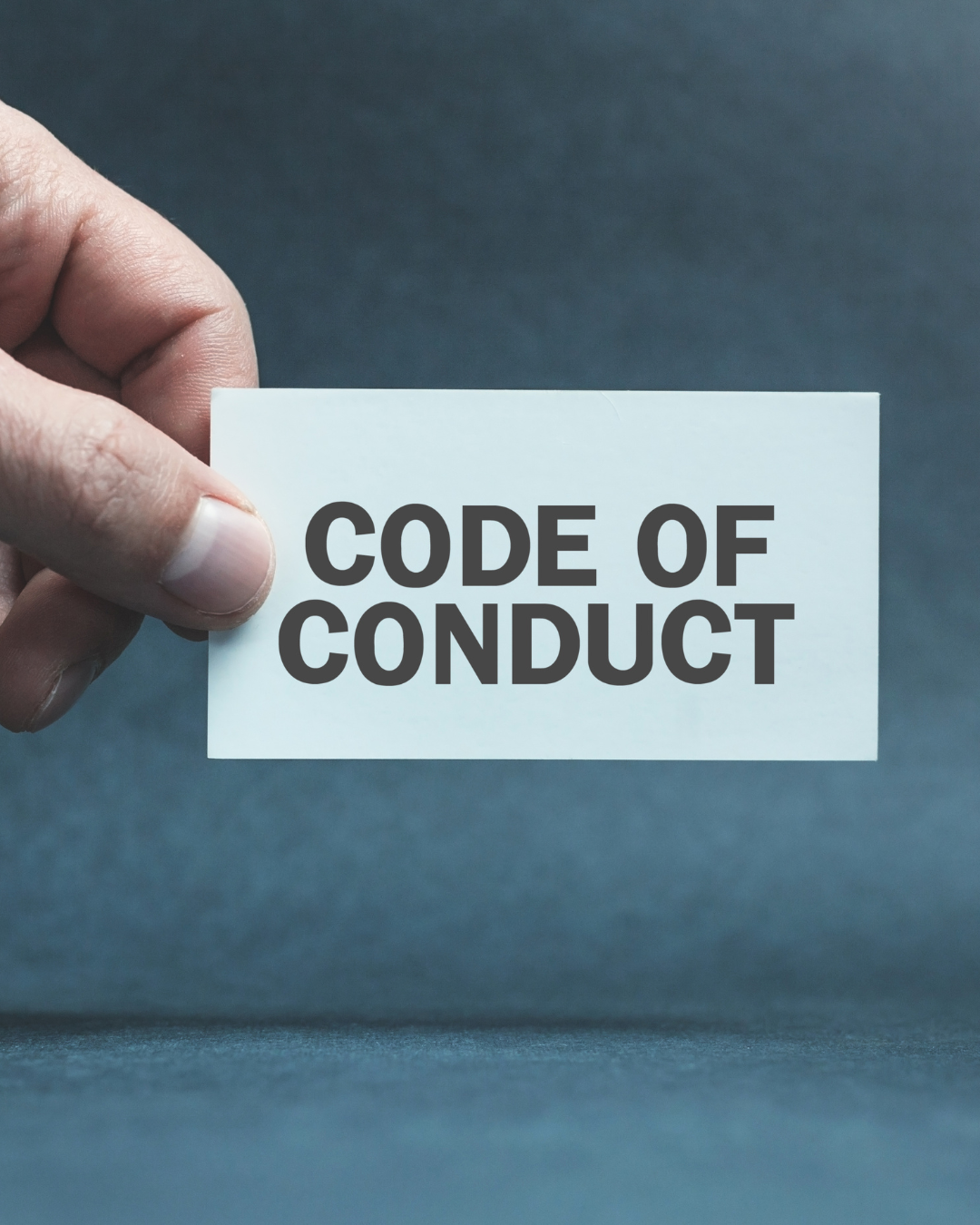Hand holding a white card with the words 'CODE OF CONDUCT' written in bold black letters against a dark background.