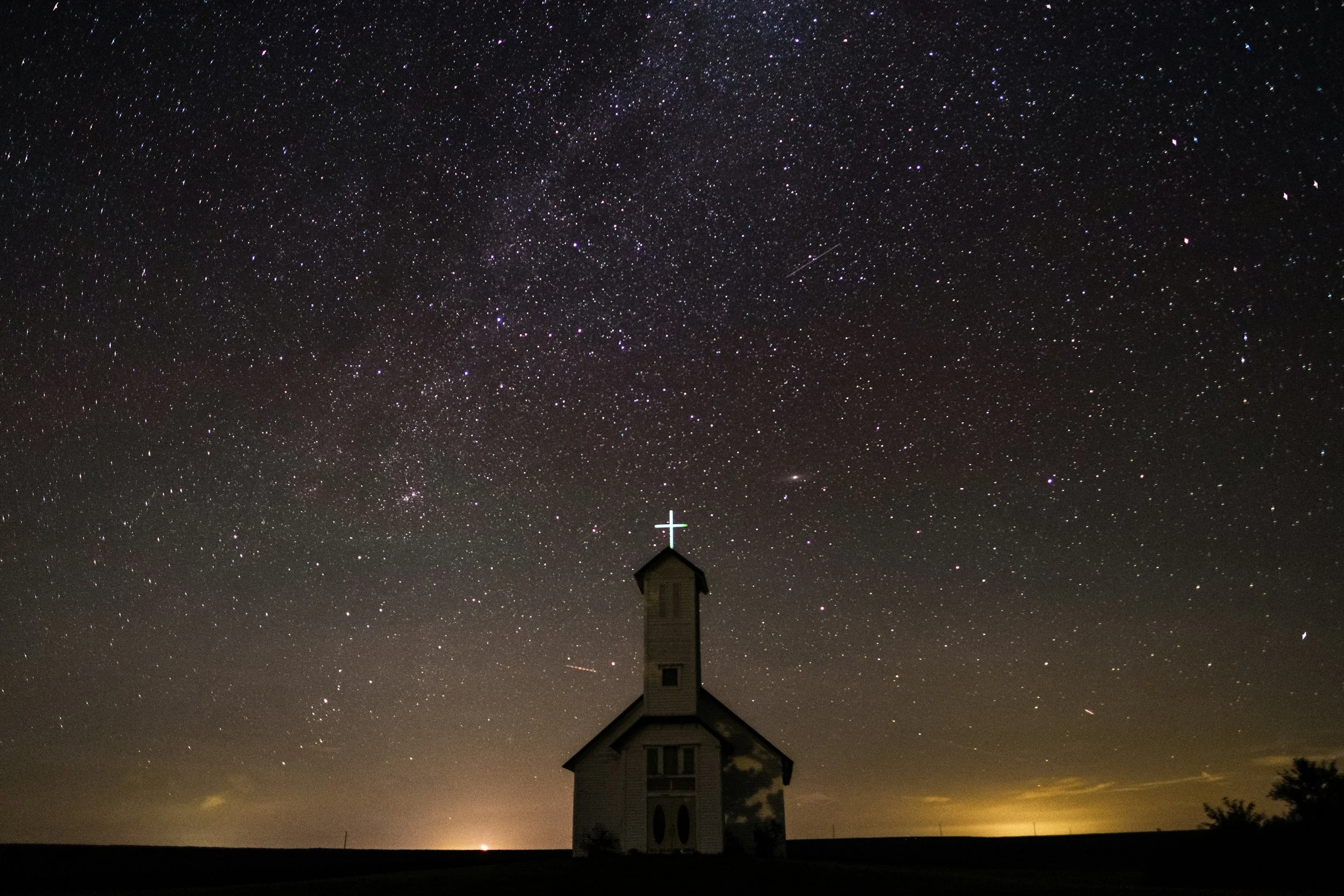Small church building with a cross on top, under a starry night sky with many visible stars.