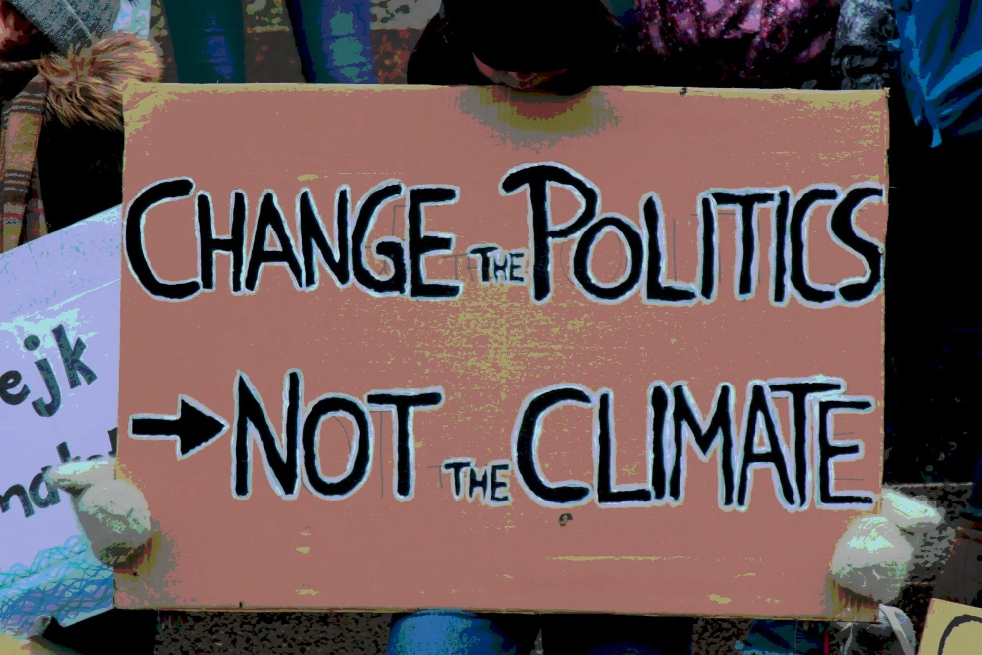 A protest sign reading 'Change the Politics, Not the Climate,' held by individuals at a rally.