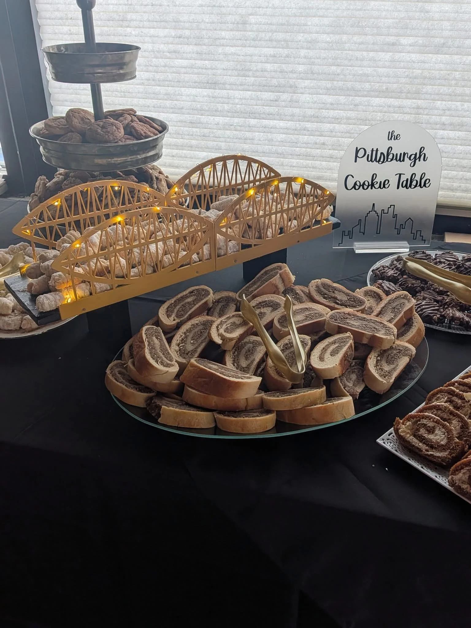 Pastry and cookie display at Pittsburgh Cooke Table event, including a large plate of rolled cookies with a swirl pattern, and a sign.