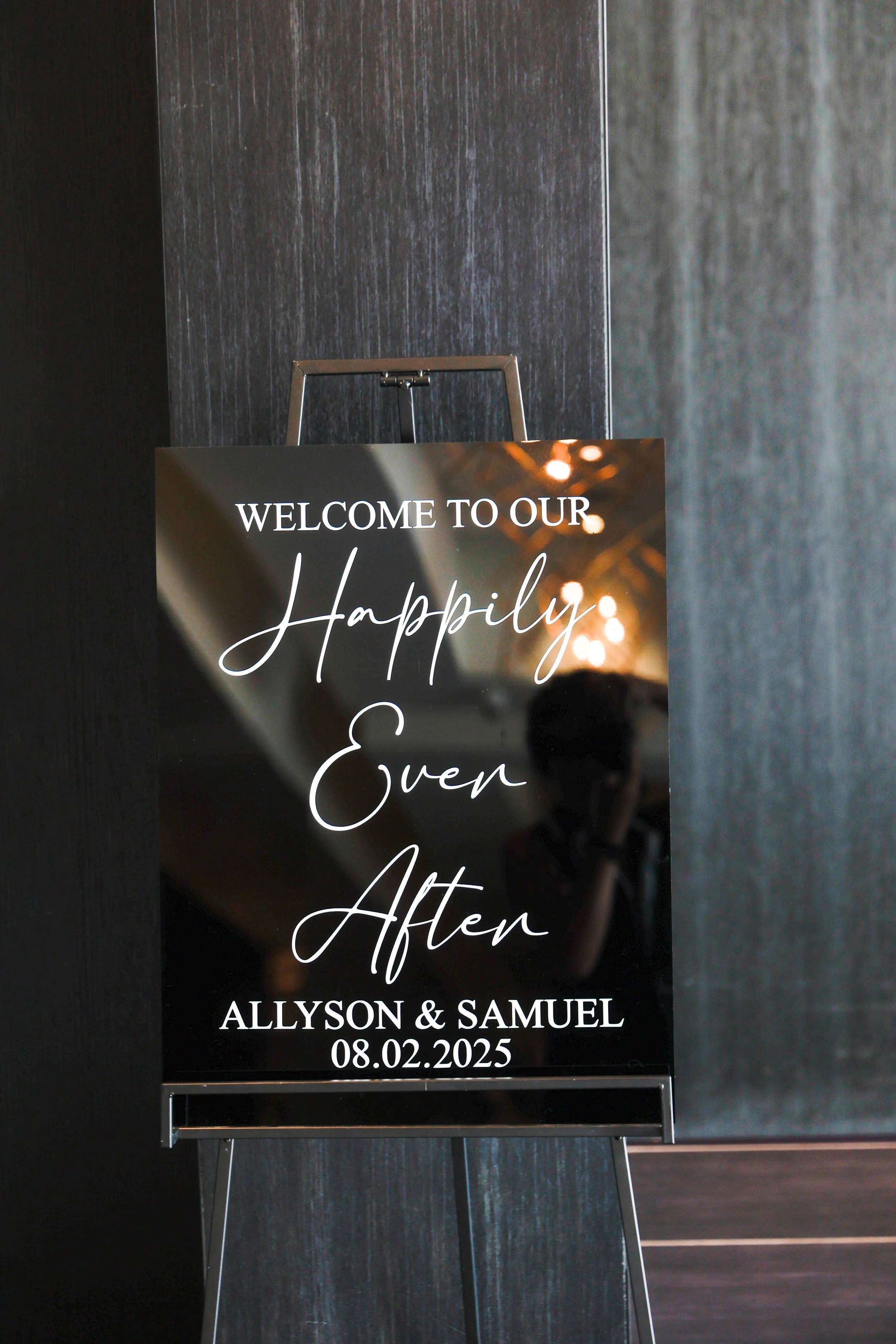 Wedding welcome sign with black background, white cursive and capitalized text, displaying the message: "Welcome to our Happily Ever After," with the names Allyson and Samuel and the date 08.02.2025.