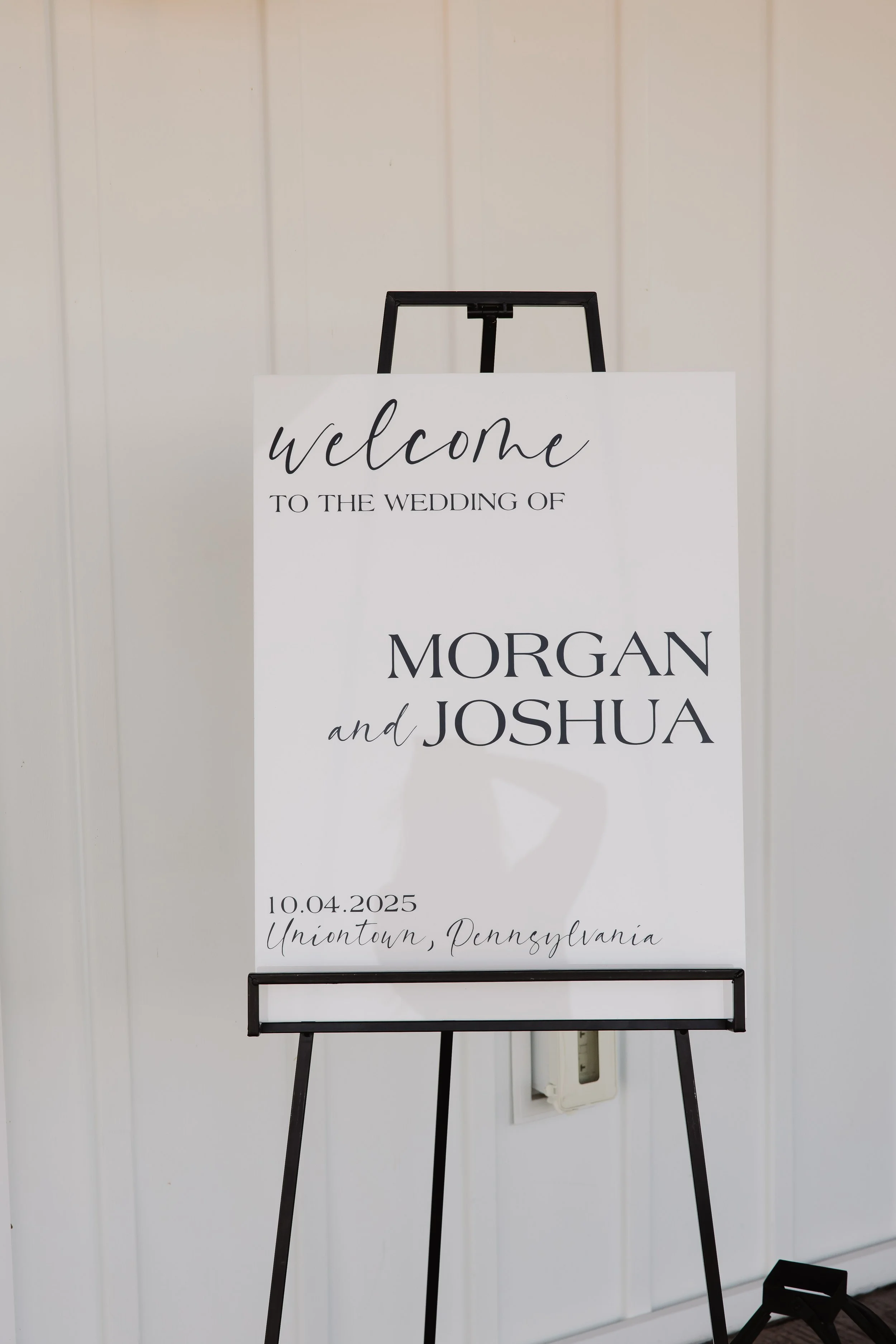 Wedding welcome sign for Morgan and Joshua, scheduled for October 4, 2025, in Uniontown, Pennsylvania, displayed on an easel against a white wall.