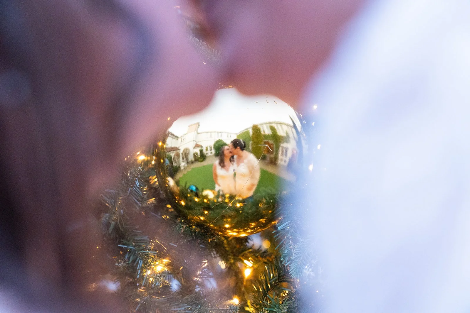 A couple taking a selfie, reflected in a gold ornament on a Christmas tree.