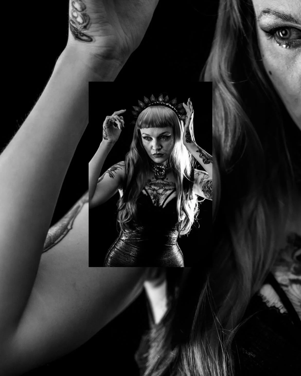 Black and white photograph of a woman with tattoos, wearing a crown and a black dress, posing with her hands near her head.